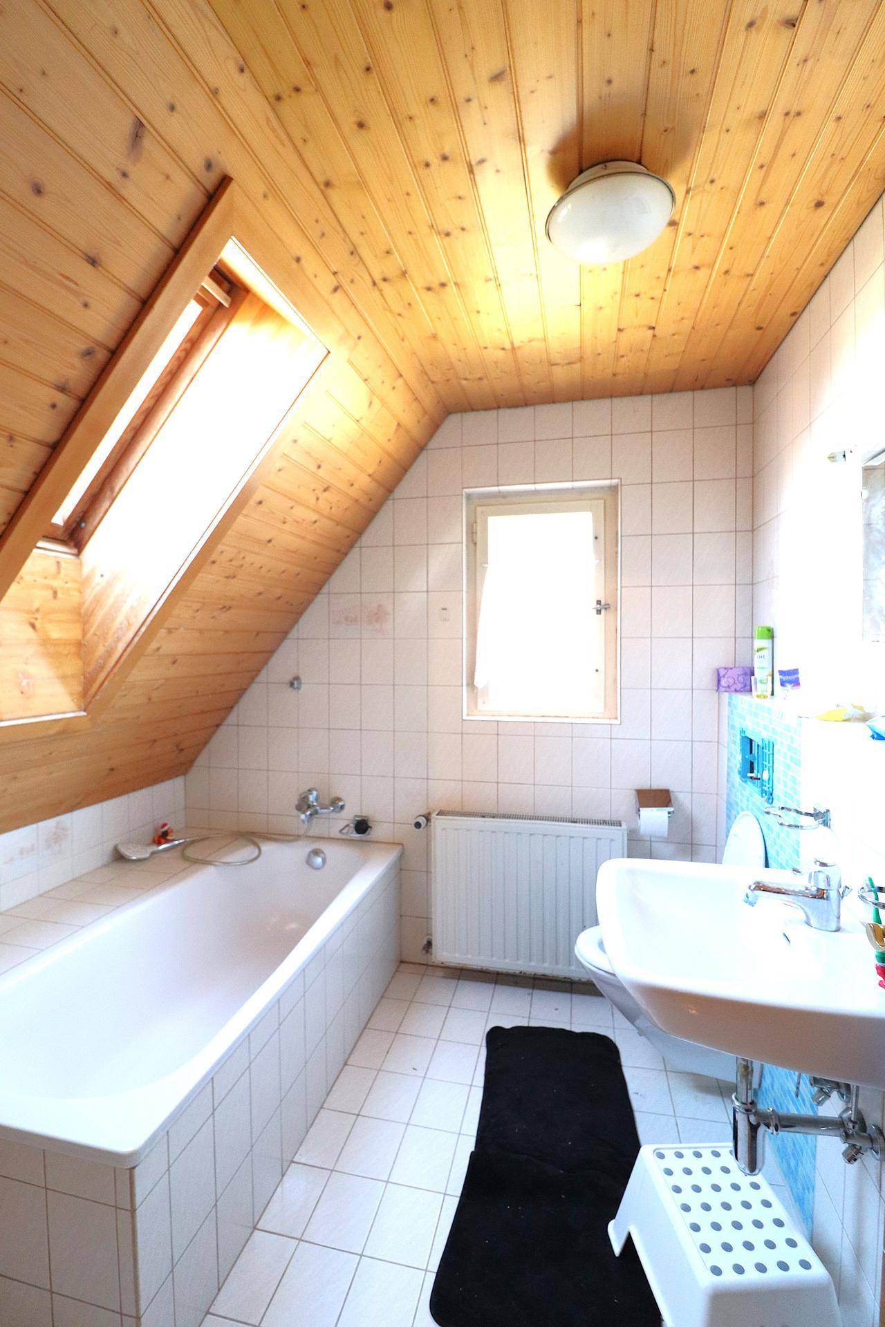 Dachgeschoss-Badezimmer mit Badewanne, Dachfenster und Holzvertäfelung an der Decke.