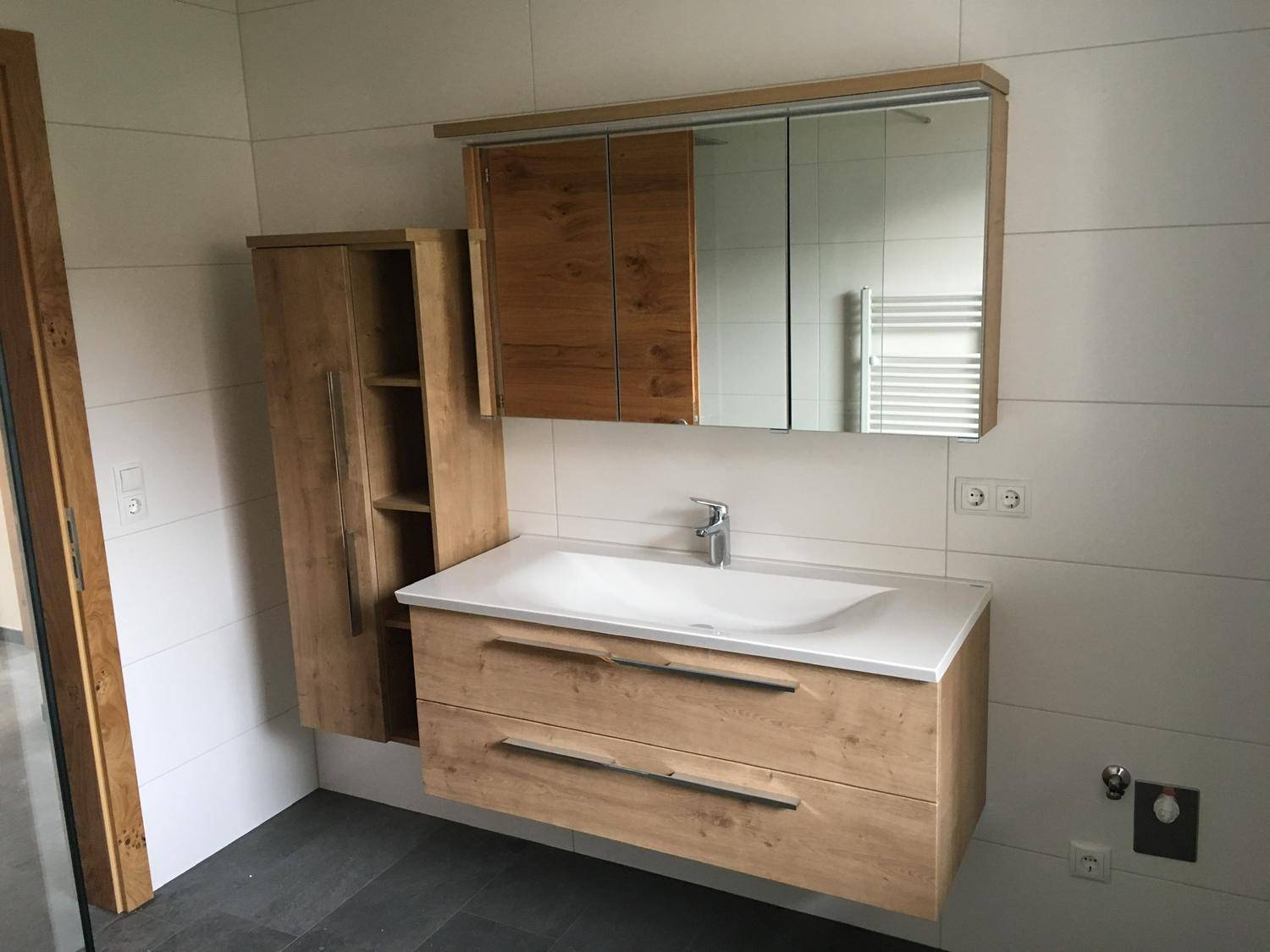 Modernes Badezimmer mit Holzwaschtischunterschrank, Spiegelschrank und weißen großformatigen Fliesen.
