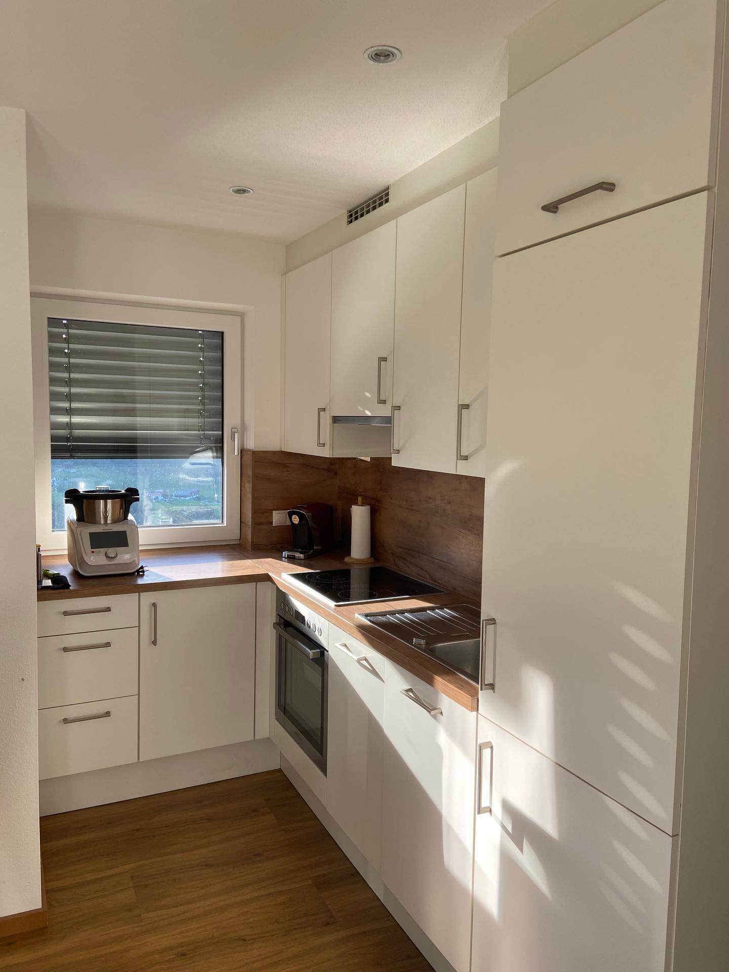 Helle, moderne Küche mit weißen Schränken, Holz-Arbeitsplatten und Fenster mit Blick ins Grüne.