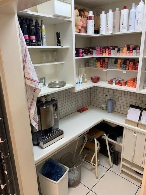 Lagerraum oder Personalbereich mit Regalen voller Haarpflegeprodukte, einer Kaffeemaschine und Arbeitsfläche.