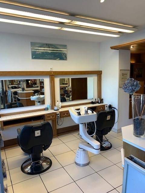 Zwei Frisierplätze mit Stühlen, Spiegeln und einem Haarwaschbecken in einem gut beleuchteten Salonbereich.