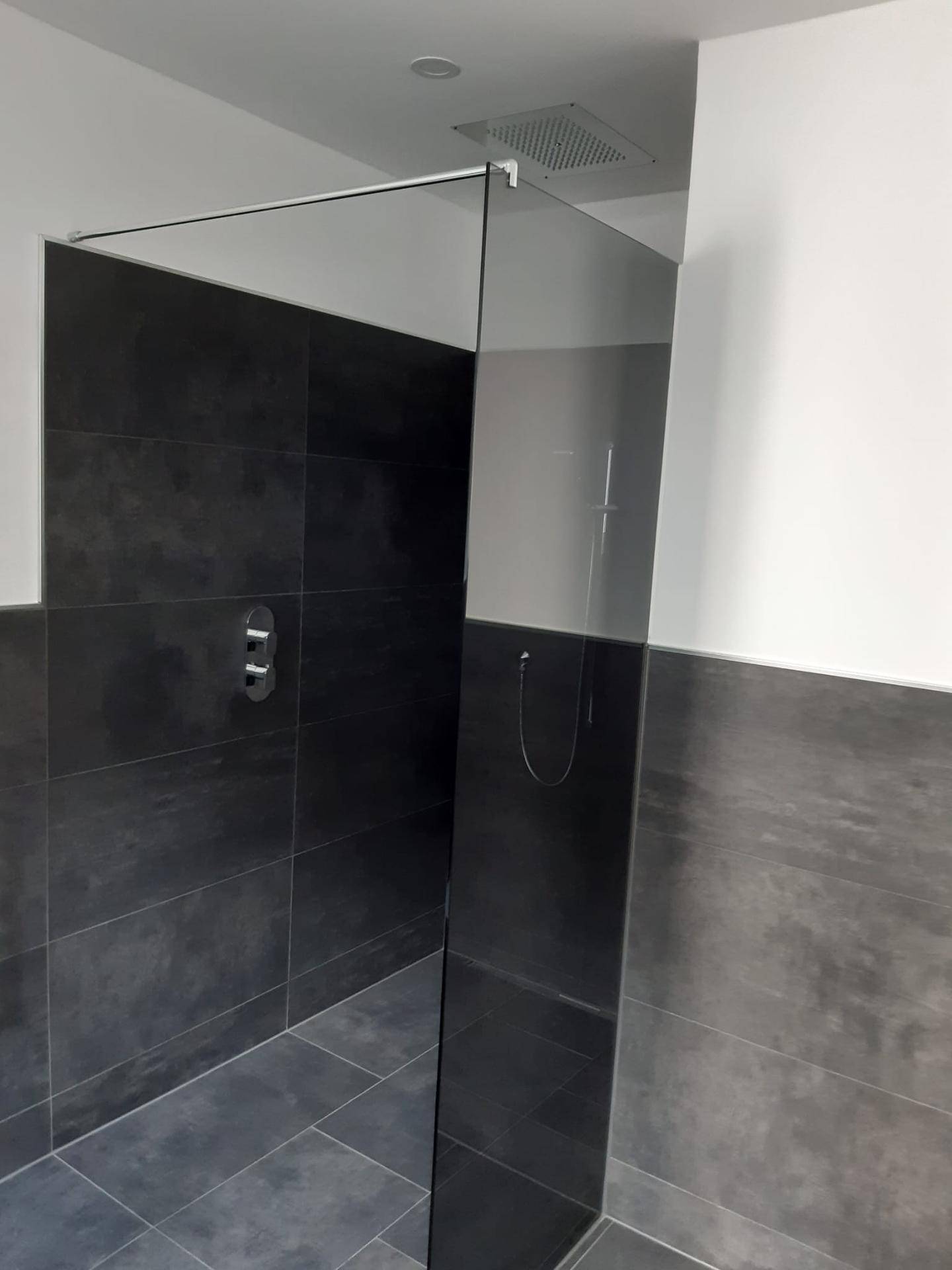 Geräumige Duschkabine mit eleganten dunklen Fliesen und einer transparenten Glasabtrennung im modernen Badezimmer.