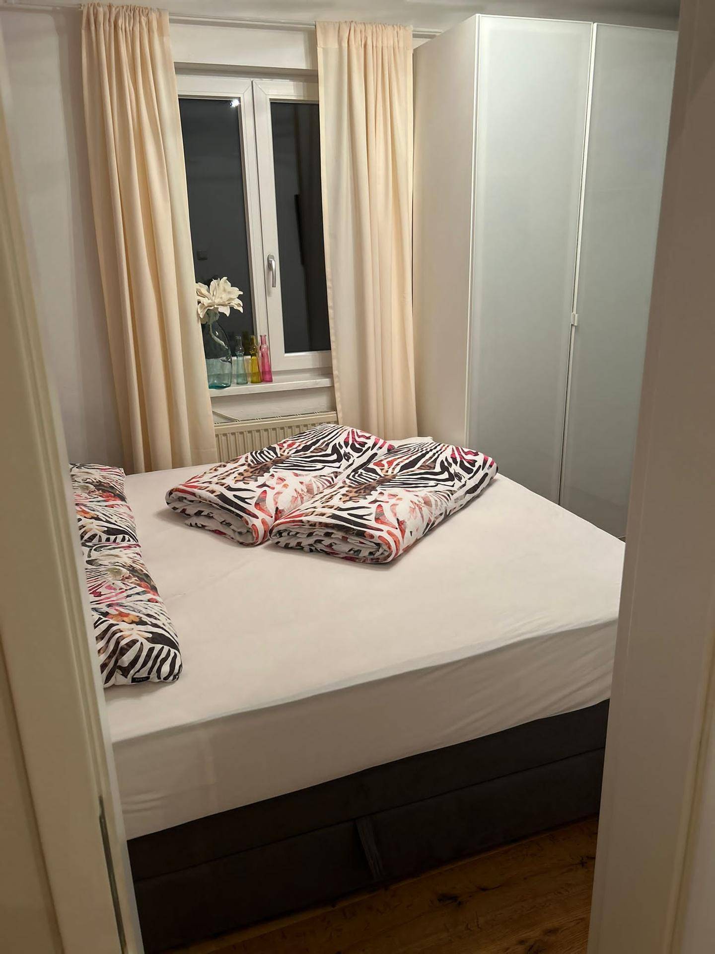 Helles Schlafzimmer mit Doppelbett, großem Kleiderschrank und Fenster mit Vorhängen.