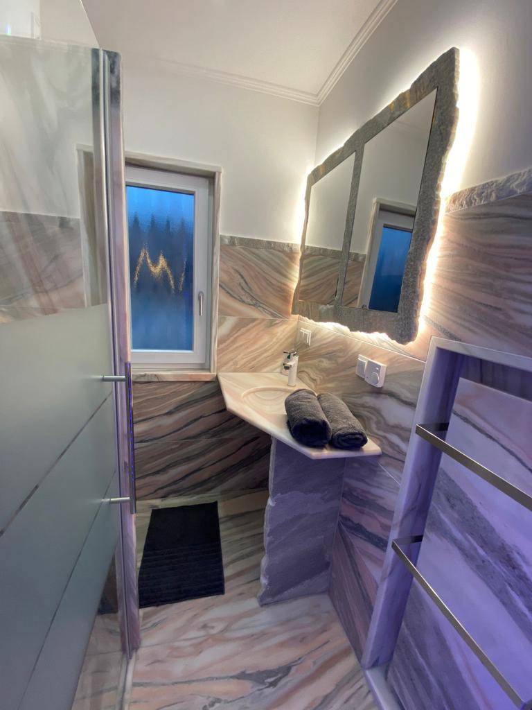 Modernes Badezimmer mit auffälligen Marmorfliesen, beleuchtetem Spiegel und integriertem Waschtisch.