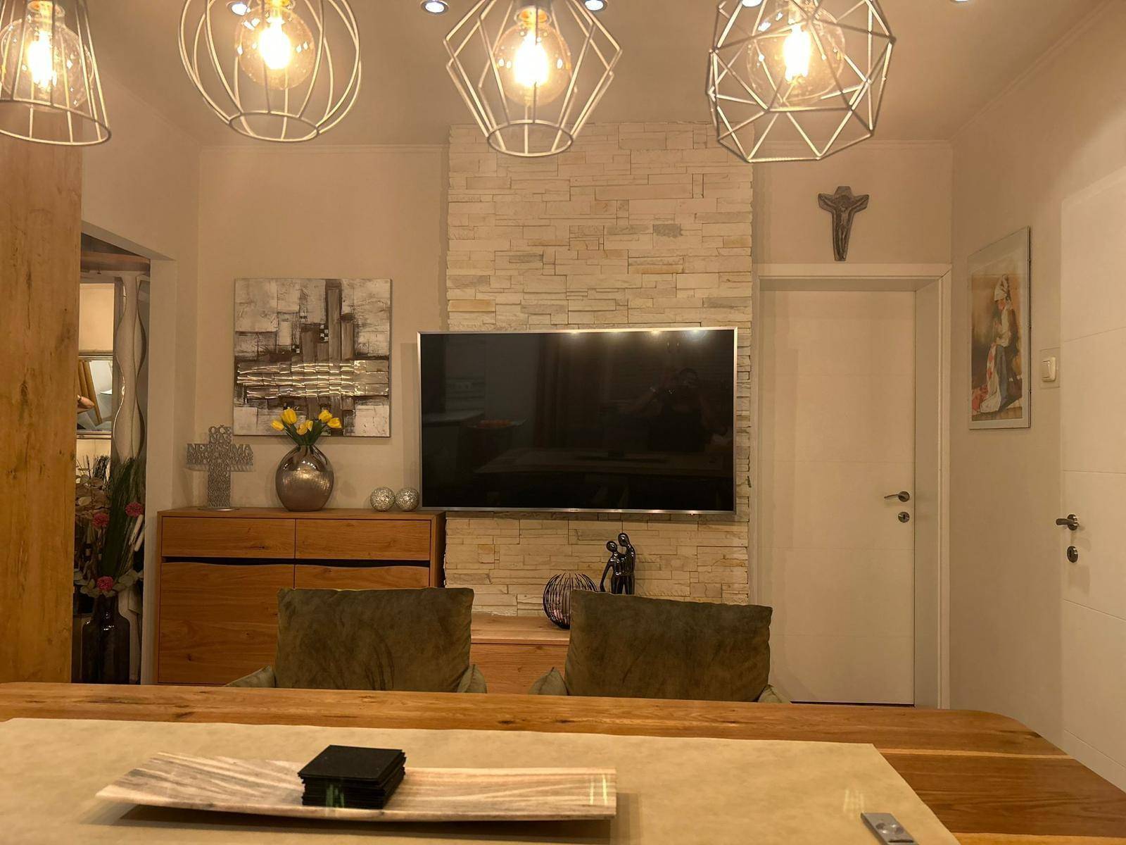Wohnbereich mit modernem Flachbildfernseher an einer dekorativen Steinwand und indirekter Beleuchtung.