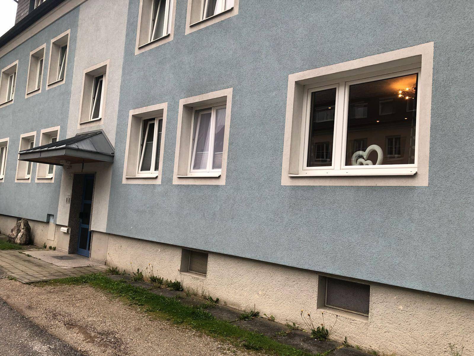 Mehrfamilienhaus mit blauer Fassade, weißen Fensterrahmen und gepflegtem Eingangsbereich.
