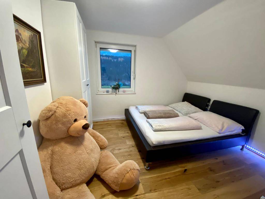 Schlafzimmer mit Dachschräge, Holzboden und einem großen Fenster, das einen Blick ins Grüne bietet.
