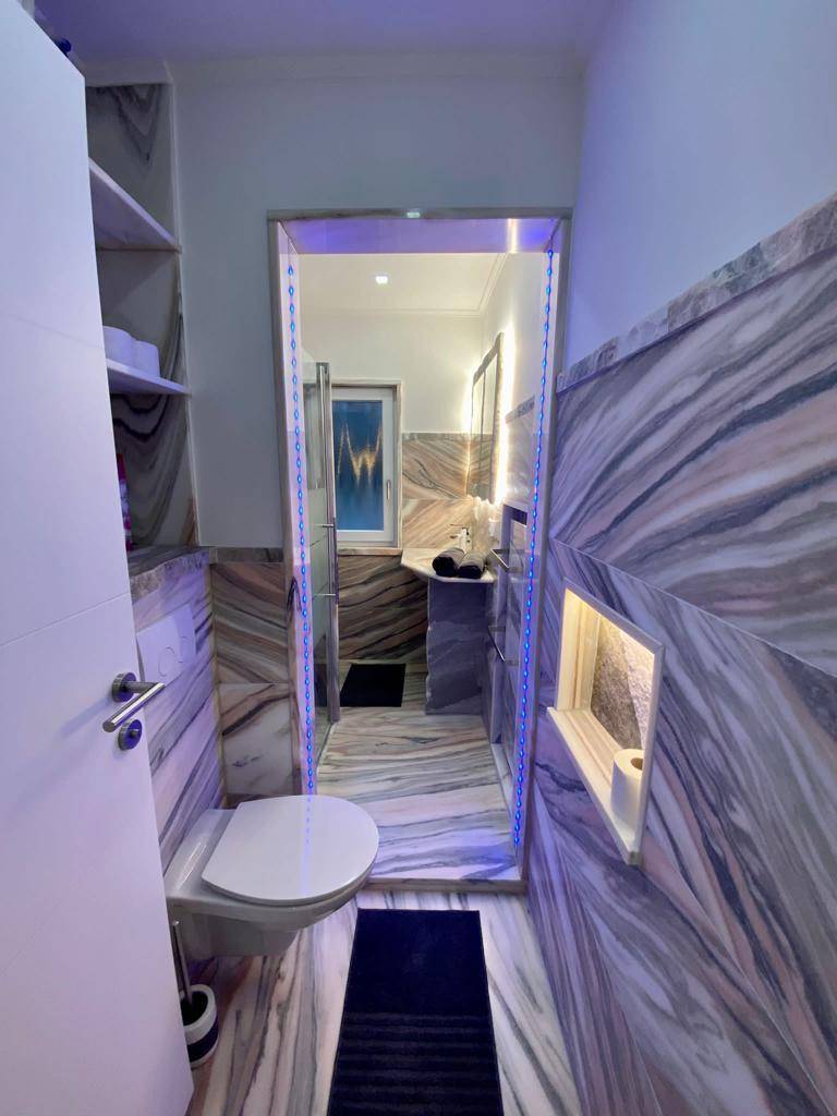 Elegantes Badezimmer mit Wand-WC, Marmorverkleidung und dekorativer Beleuchtung am Eingangsbereich.