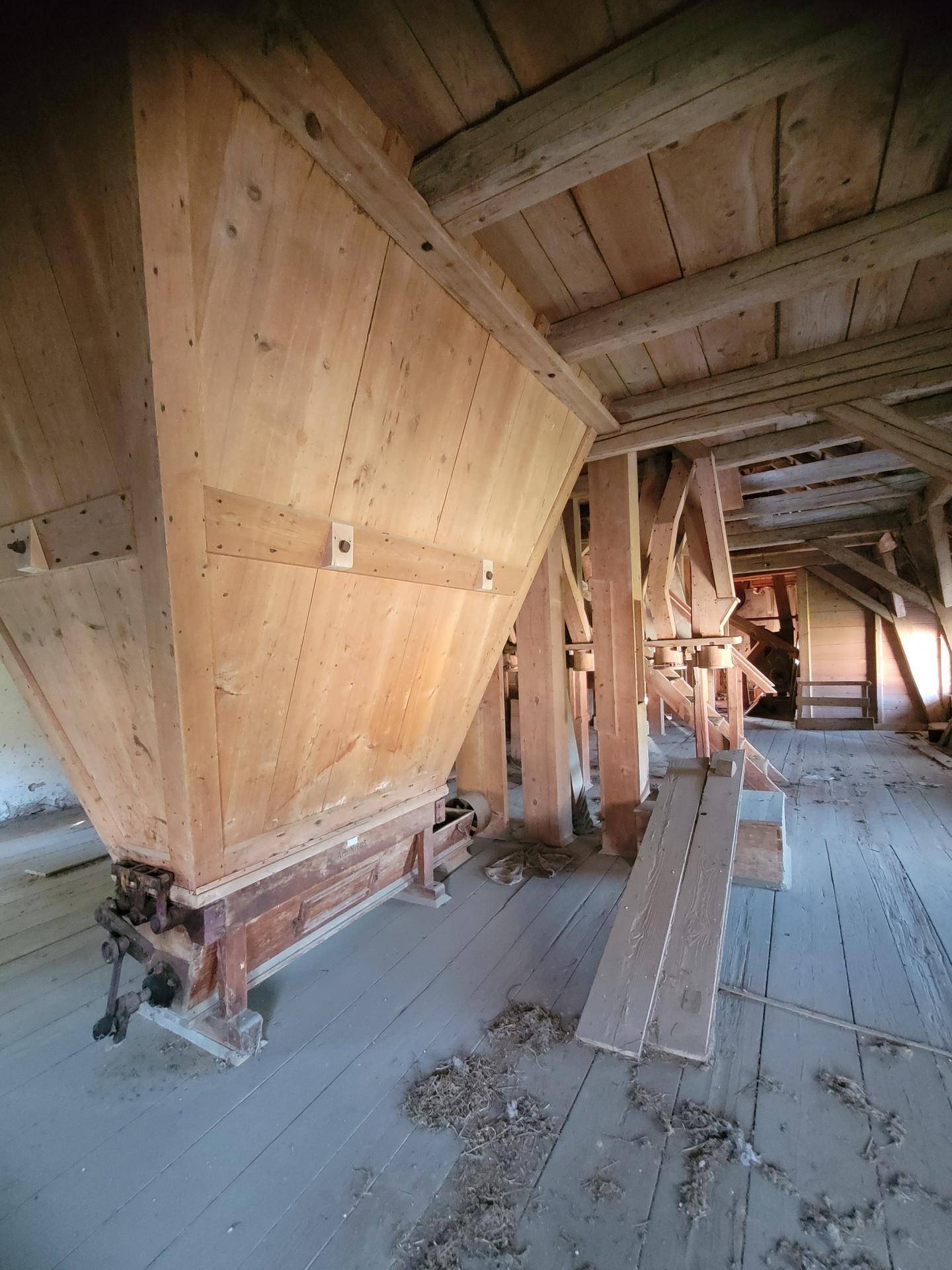 Innenansicht eines alten Mühlengebäudes mit Holzbalken, Holzfußboden und großen Holztrichtern.