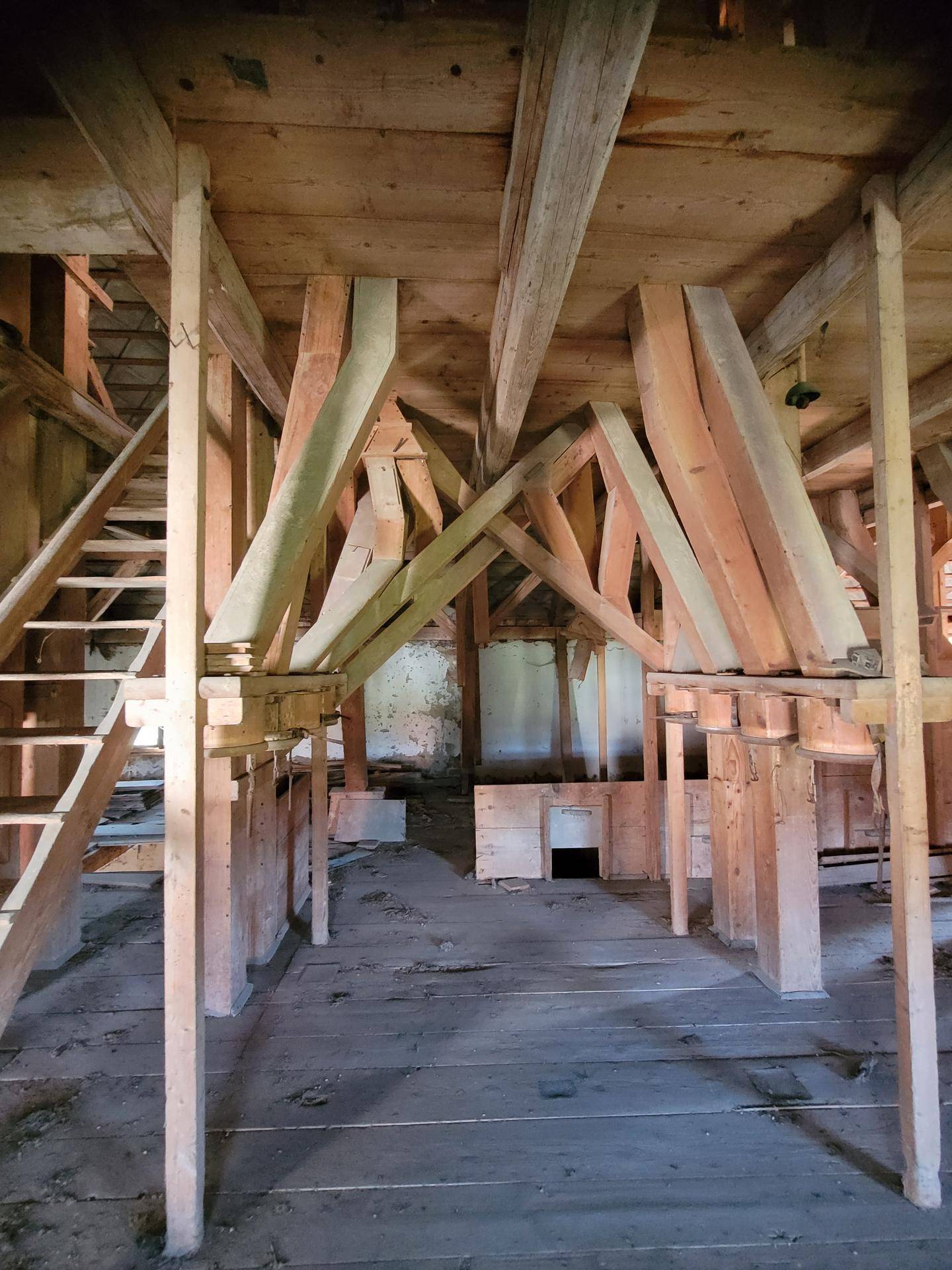 Geräumiger Innenraum eines alten Gebäudes mit komplexer Holzkonstruktion und Treppenaufgang.
