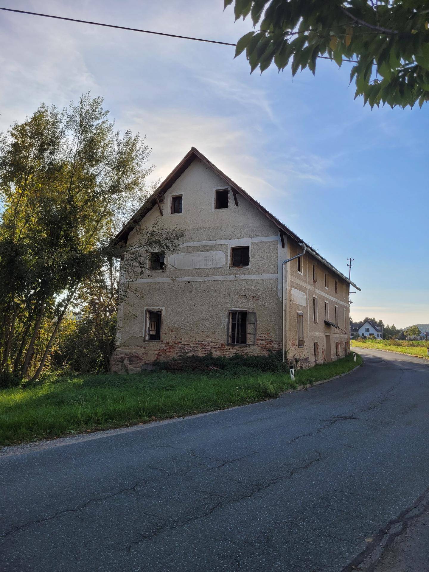 Historisches Gebäude mit Putzfassade und Satteldach an einer ländlichen Straße gelegen.