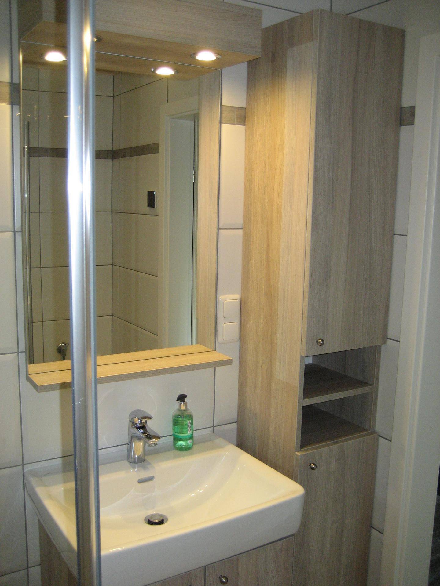 Waschbeckenbereich im Badezimmer mit Spiegelschrank, integrierter Beleuchtung und Holzdetails.