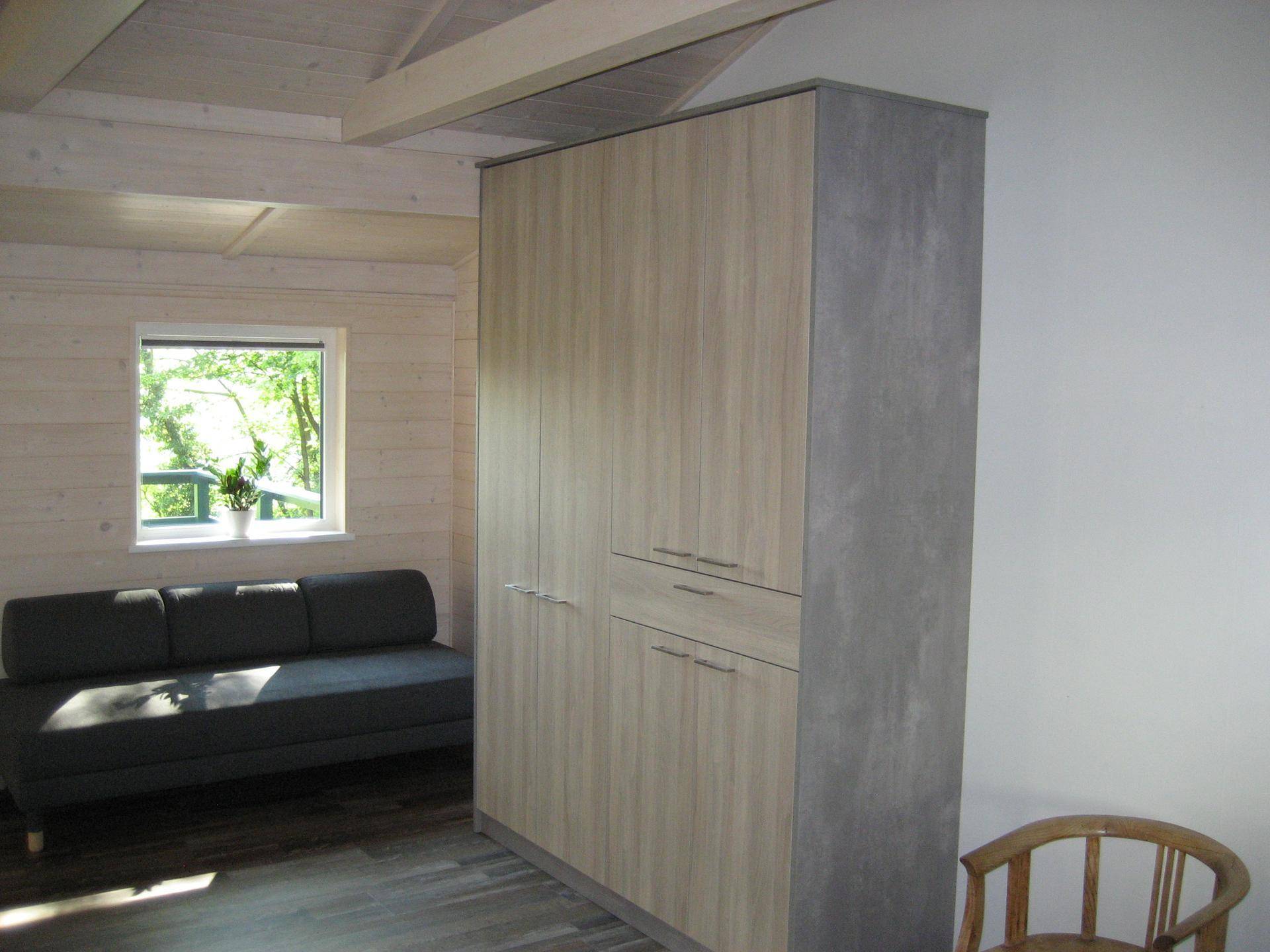 Heller Wohnraum mit Holzvertäfelung, bequemer Couch und großem Einbauschrank, mit Waldblick.