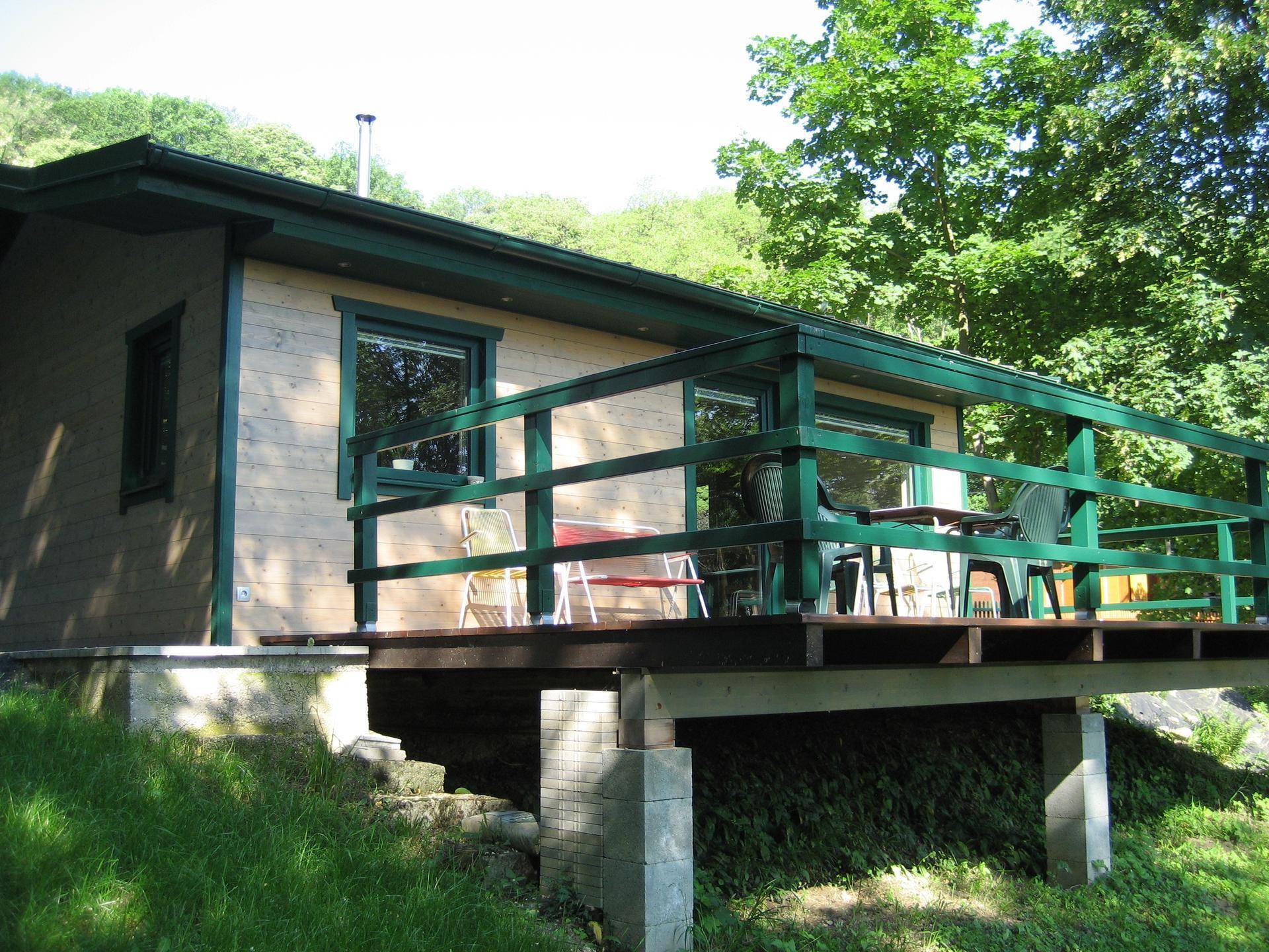 Holzhaus mit erhöhter Holzterrasse und grüner Brüstung, ideal für entspannte Stunden im Freien.