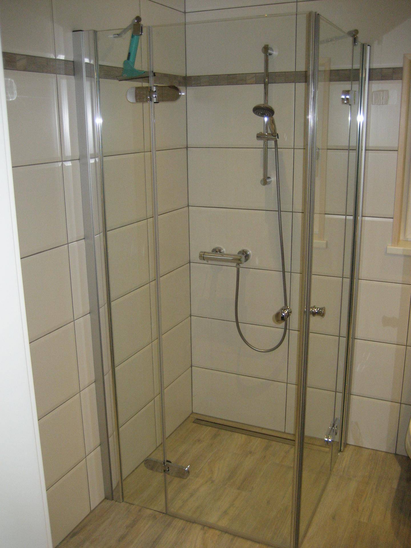 Moderne Duschkabine mit Glaswänden und hellem Fliesenboden, sauber und funktional.