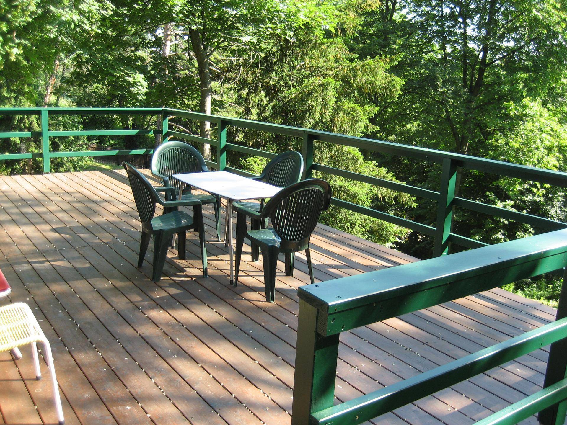 Geräumige Holzterrasse mit grünen Gartenmöbeln, perfekt für Mahlzeiten im Freien mit Waldblick.