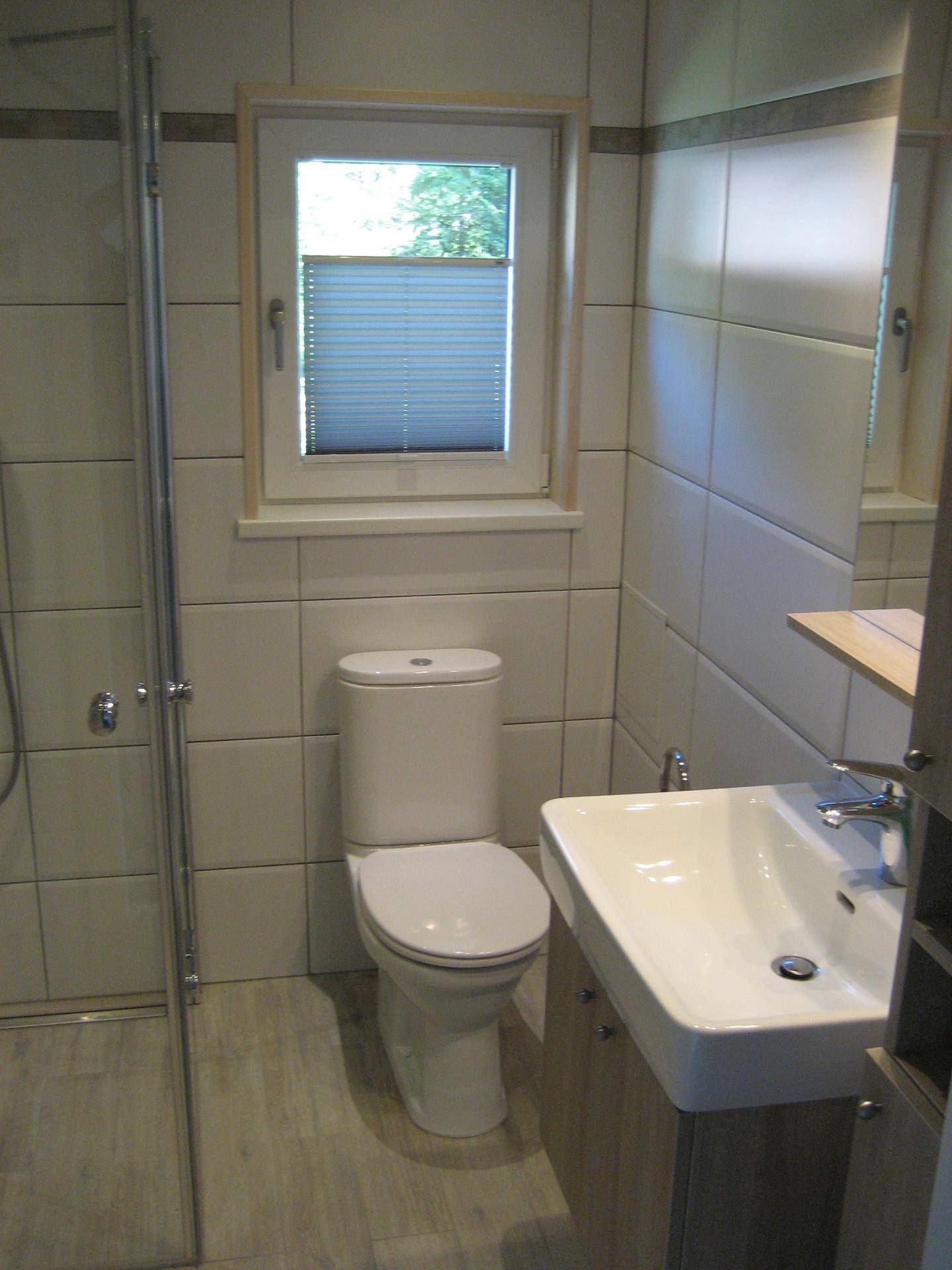 Helles Badezimmer mit WC, Waschbecken und Fenster, ausgestattet mit modernen Fliesen und Armaturen.