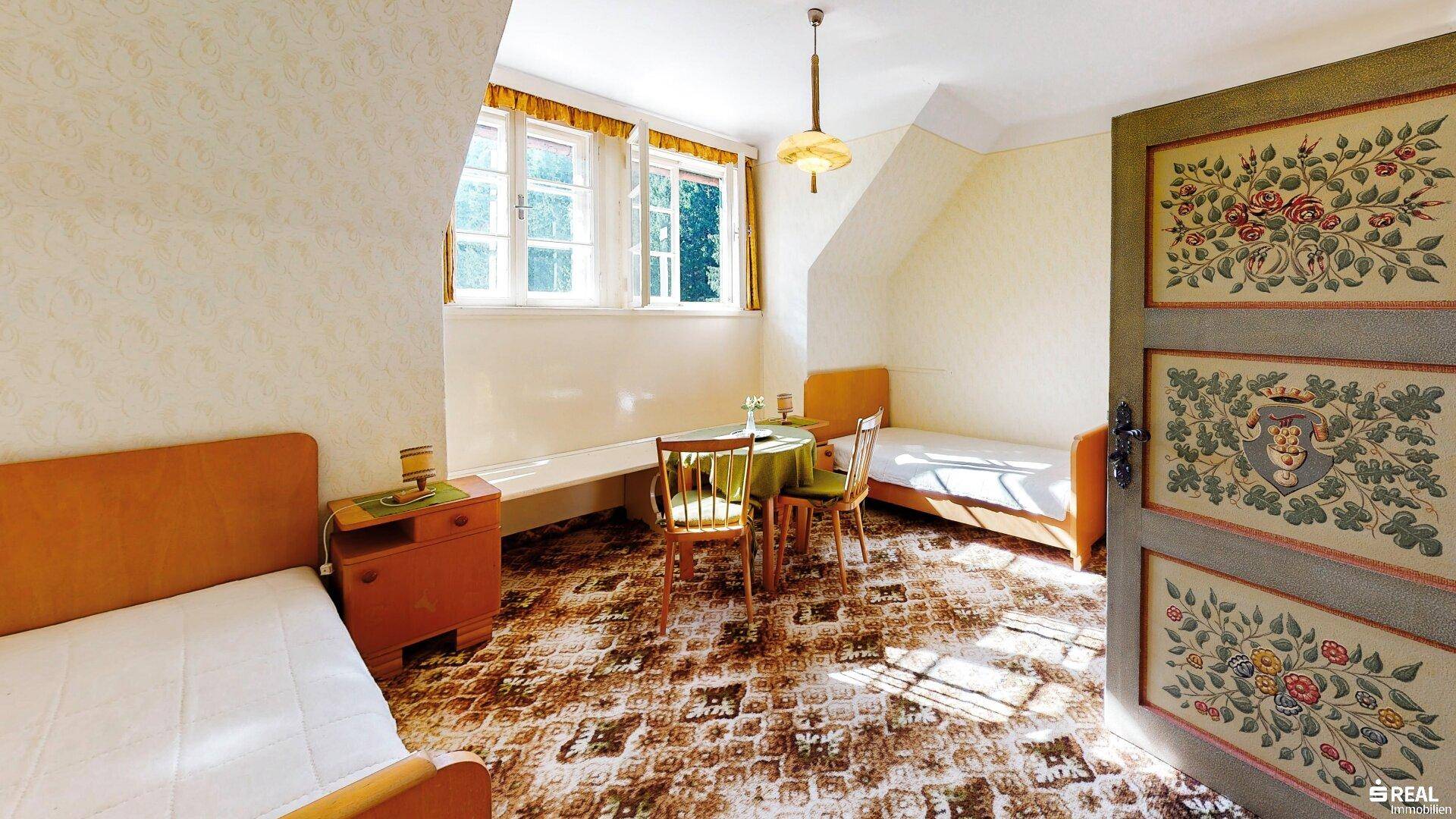 Helles Schlafzimmer mit Einzelbetten, gemustertem Teppich und traditionell bemalter Tür.