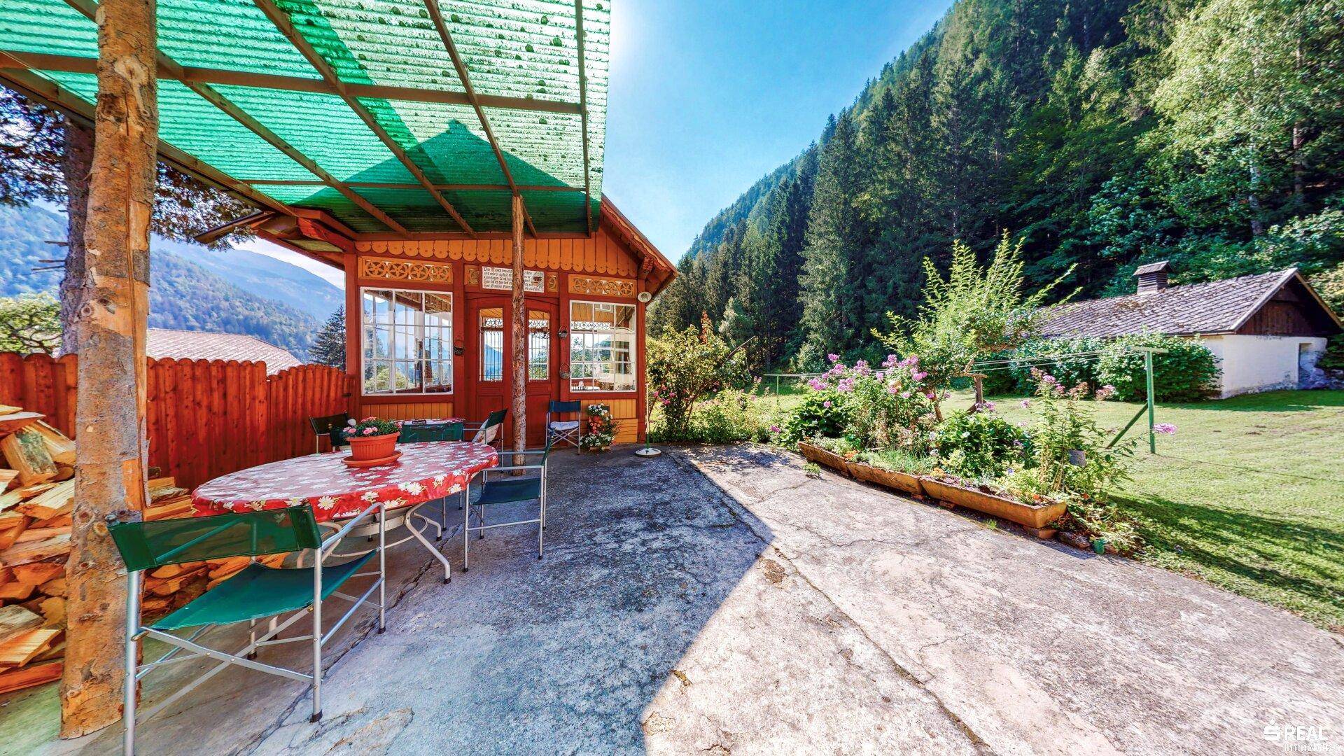 Sonniger Außenbereich mit überdachter Terrasse, Sitzgelegenheiten und Bergblick.