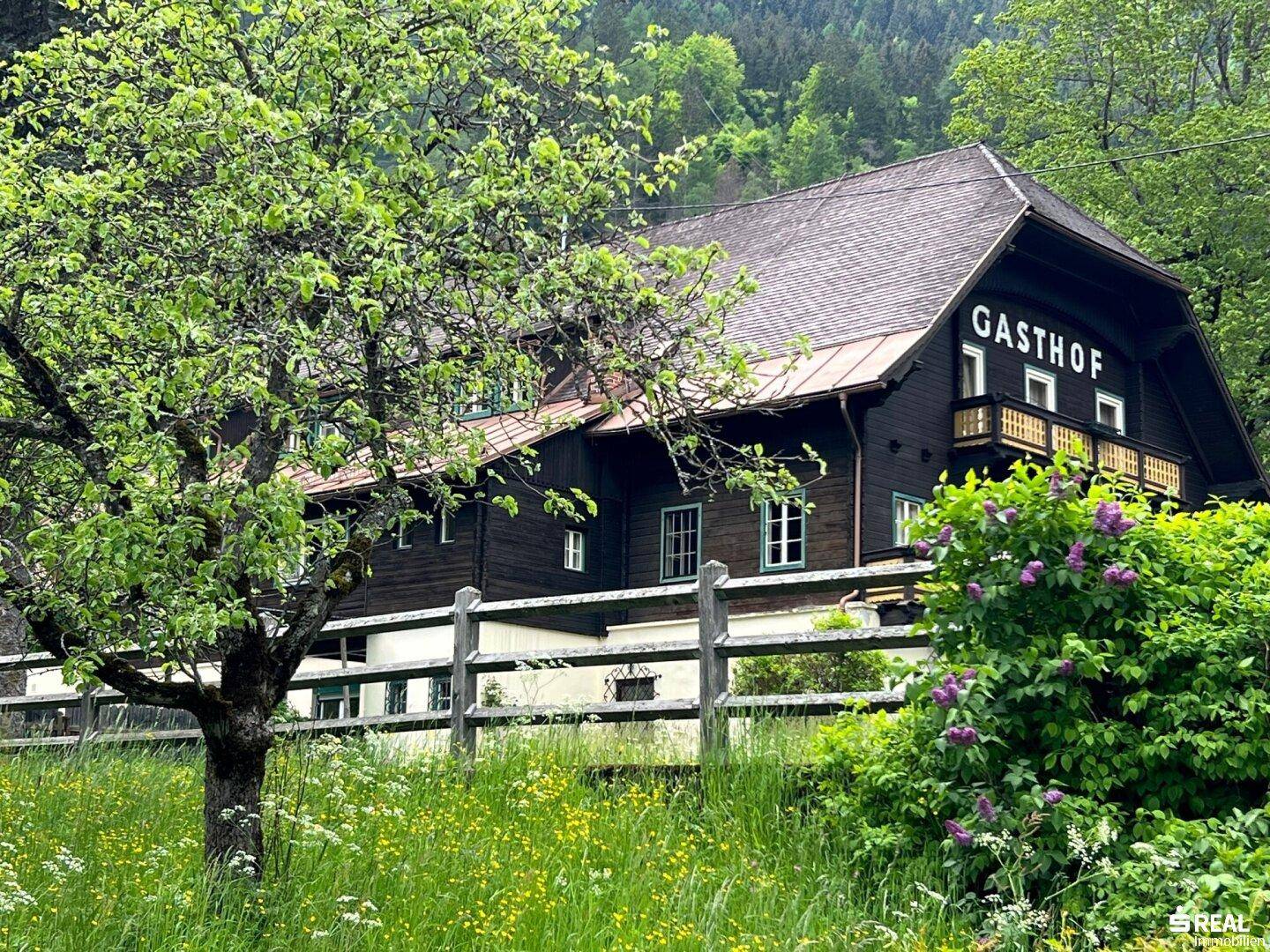 Traditionelles Gasthaus umgeben von grüner Natur und Bäumen in alpiner Landschaft.