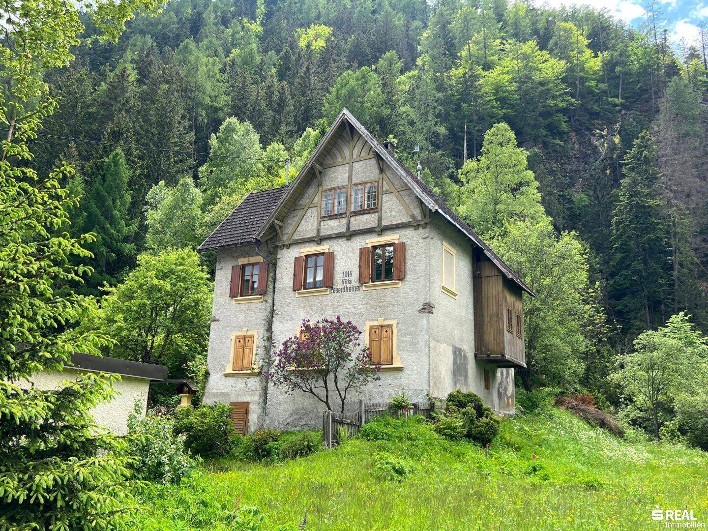 Altes Gebäude mit traditioneller Architektur, Holzbalkonen und grüner Umgebung in den Bergen.