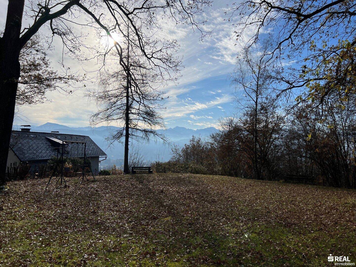 Weitläufige Landschaft mit Bergblick und einem Haus im Vordergrund unter blauem Himmel.