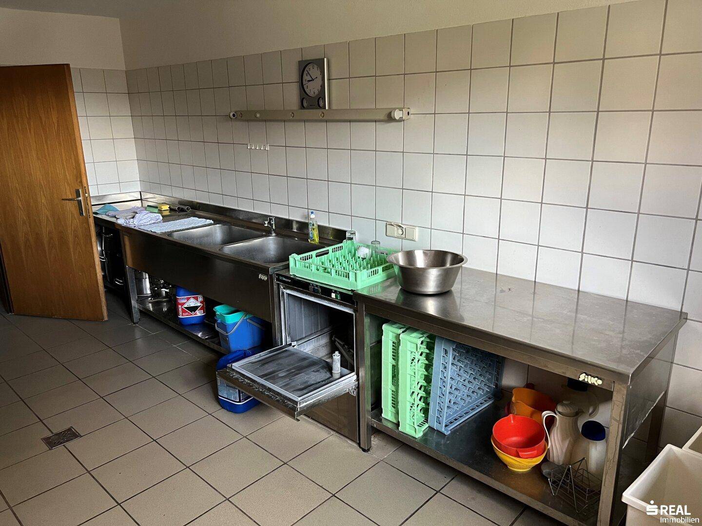 Funktionale Großküche mit Edelstahlmöbeln, Spülbecken und Industriespülmaschine für den Gastronomiebetrieb.