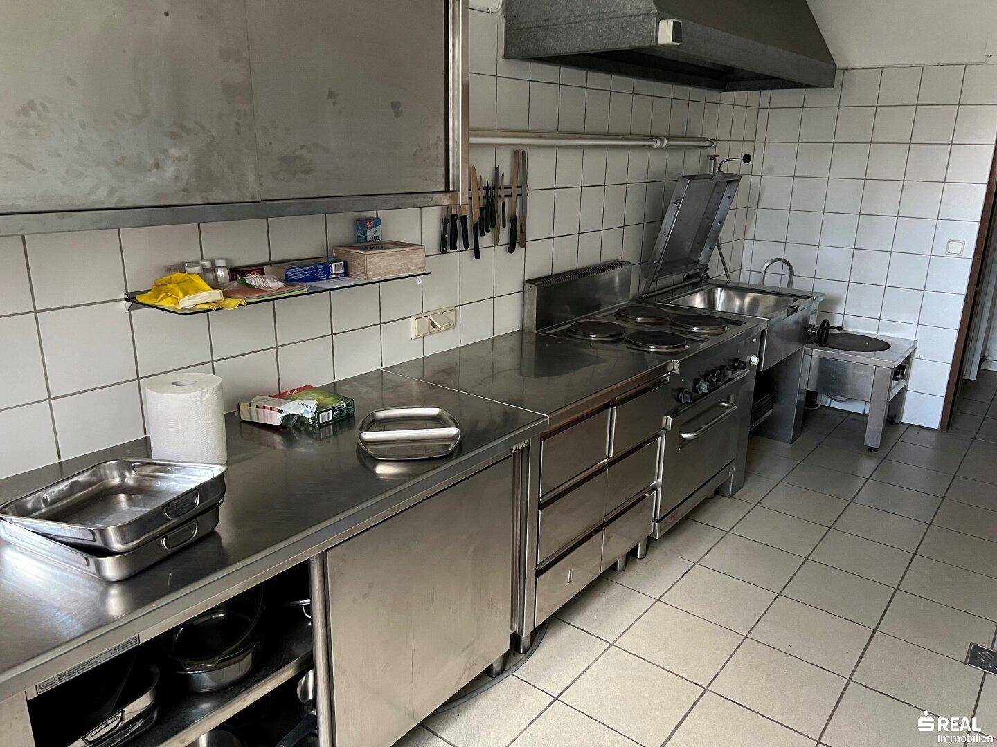Professionelle Küche mit Edelstahl-Arbeitsflächen, großem Herd und Dunstabzugshaube für die Zubereitung.