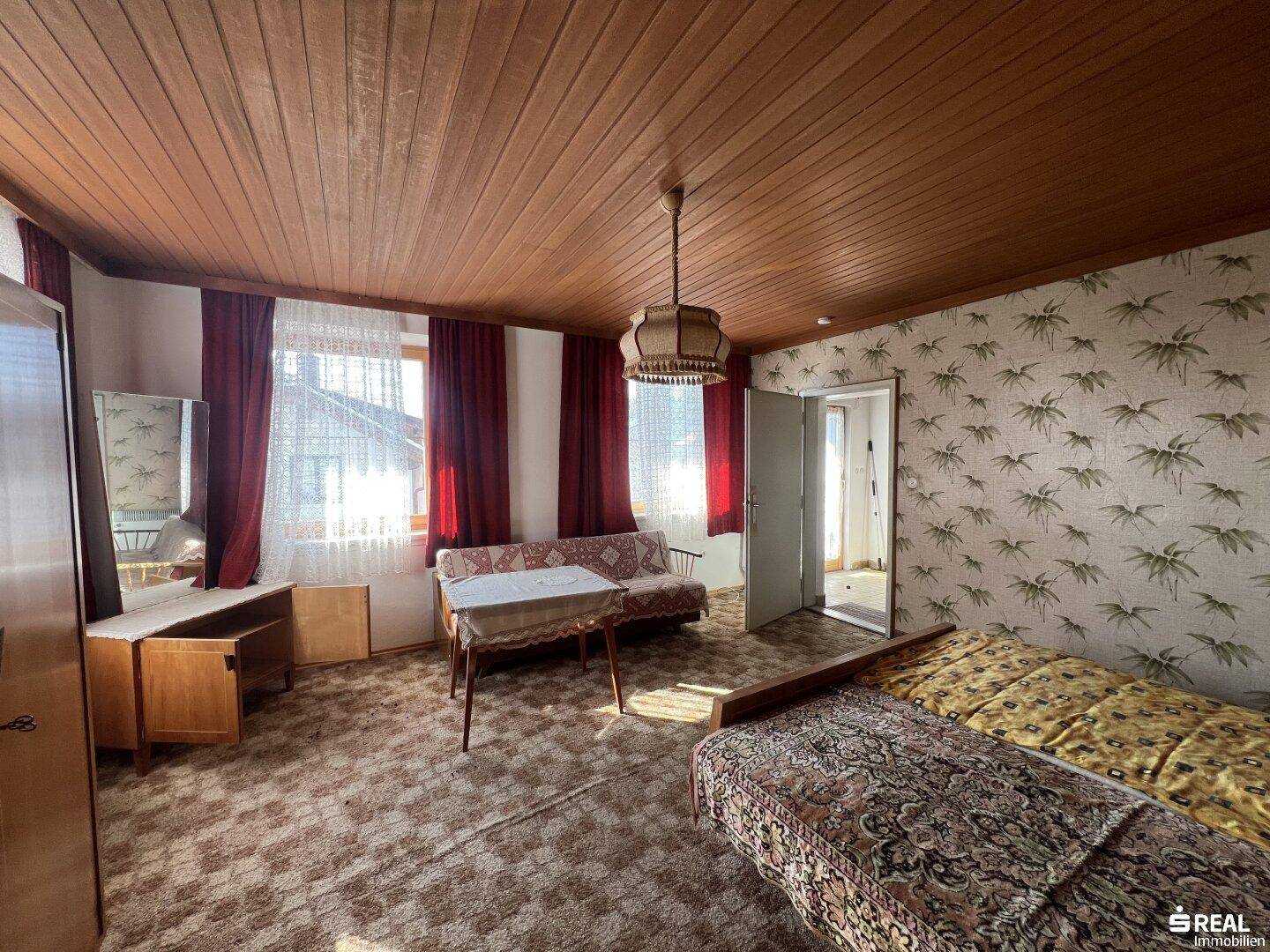 Helles Schlafzimmer mit Holzdecke, Teppichboden und Zugang zu einem weiteren Raum.
