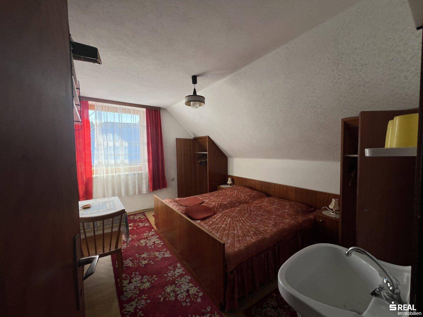 Dachgeschoss-Schlafzimmer mit schrägen Wänden, Teppichboden und Waschbecken.