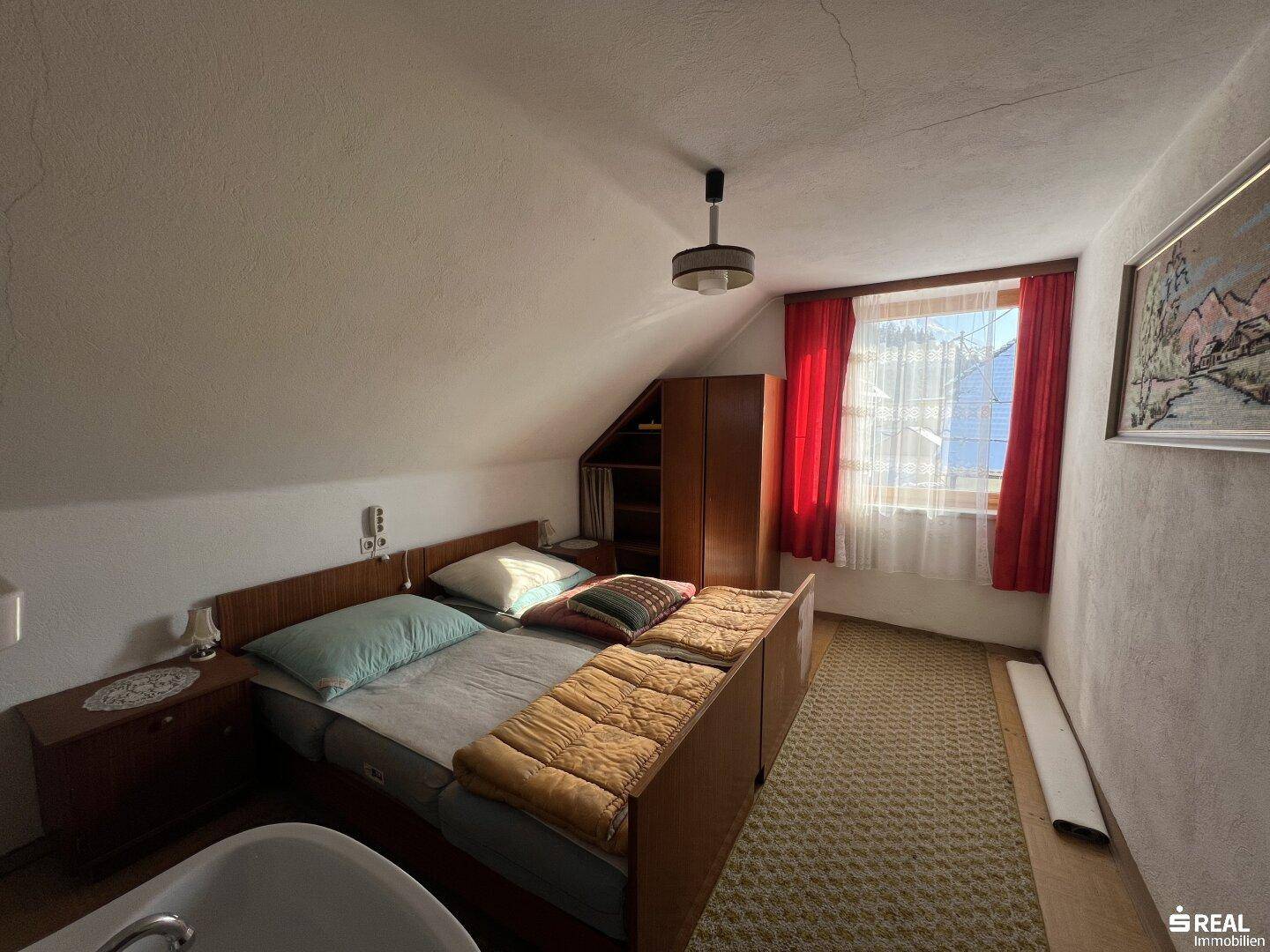 Schlafzimmer im Dachgeschoss mit schrägen Wänden, Teppichboden und Doppelbett.
