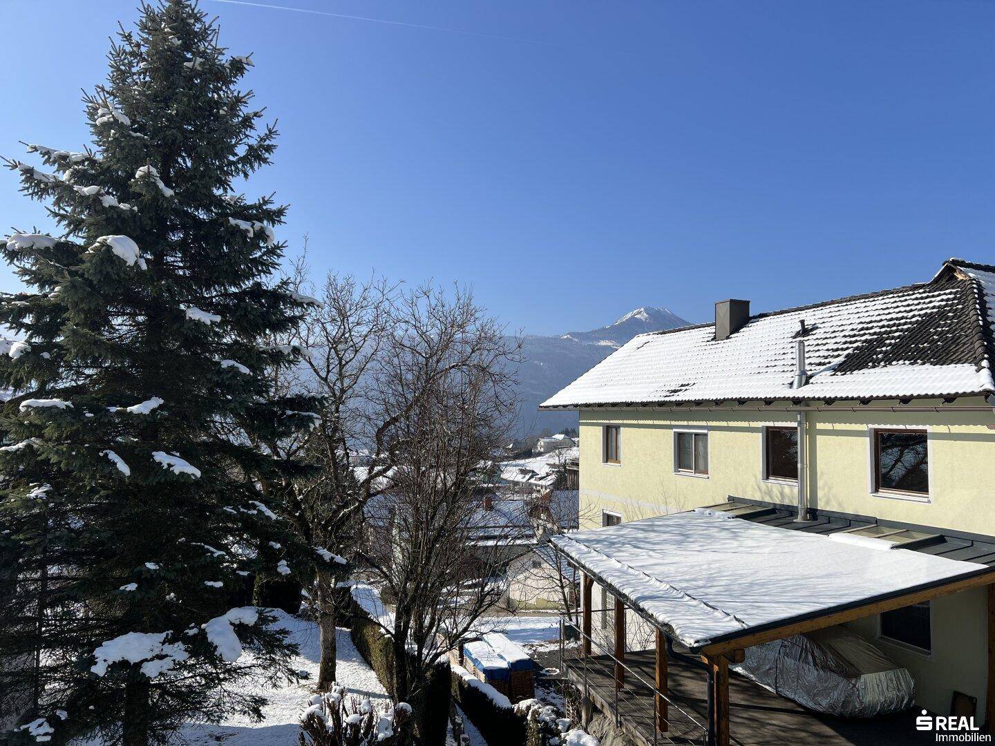 Winterliche Landschaft mit verschneiten Bäumen und Häusern, im Hintergrund Berge.