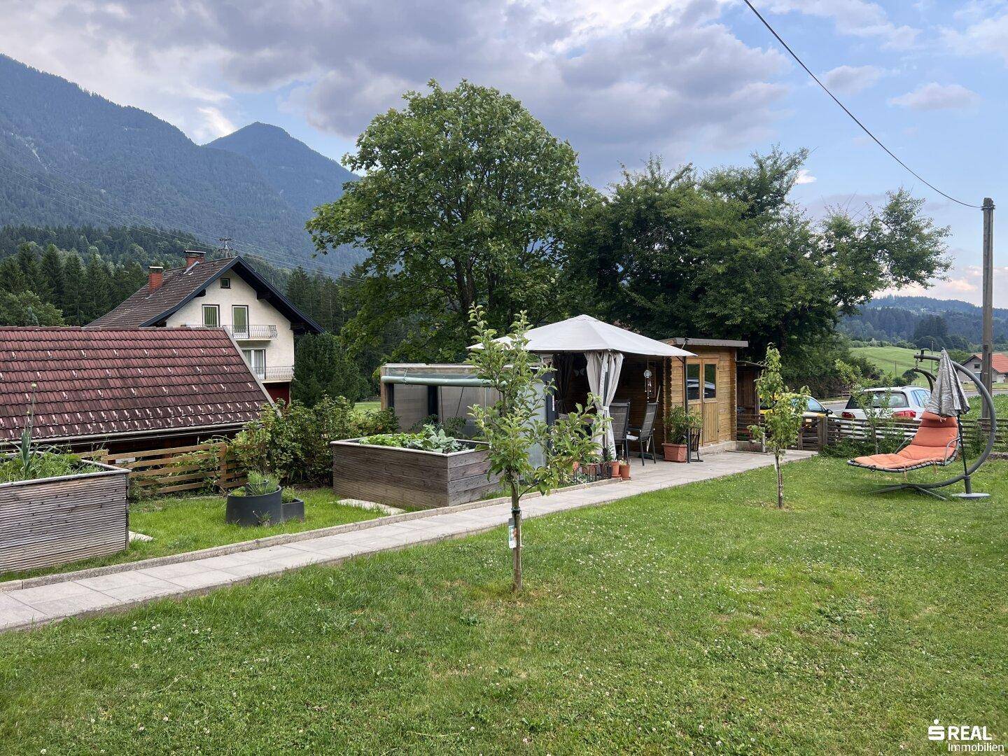 Weitläufiger Gartenbereich mit Gartenhaus, Schaukelstuhl und Blick auf die umliegende Berglandschaft.