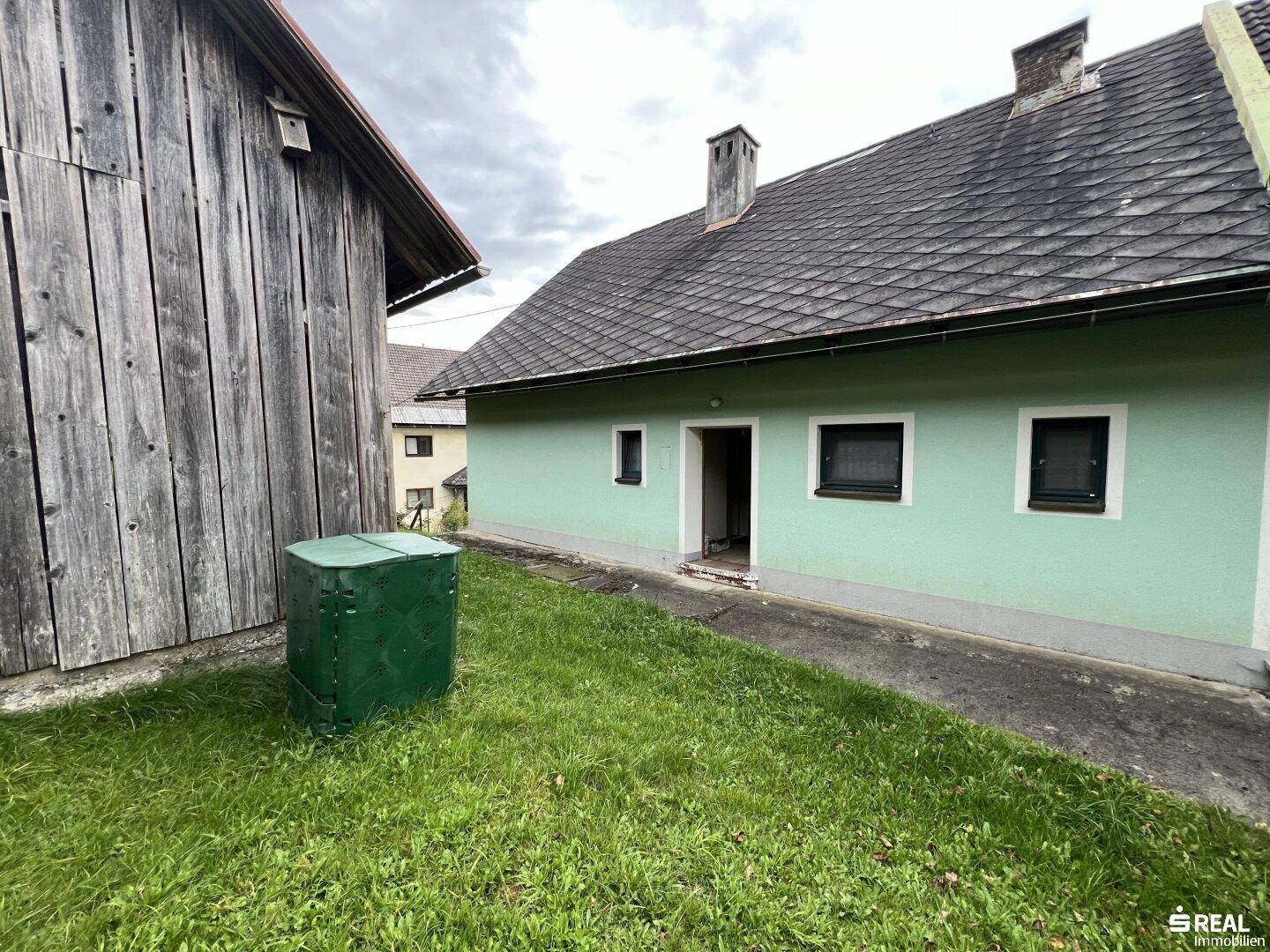Hinterhofbereich mit Rasenfläche und einem Nebengebäude aus Holz.