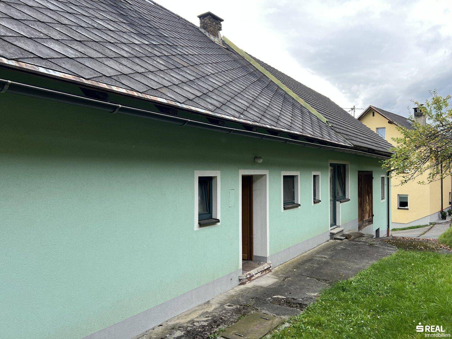 Seitenansicht des Hauses mit grüner Fassade und mehreren Fenstern.