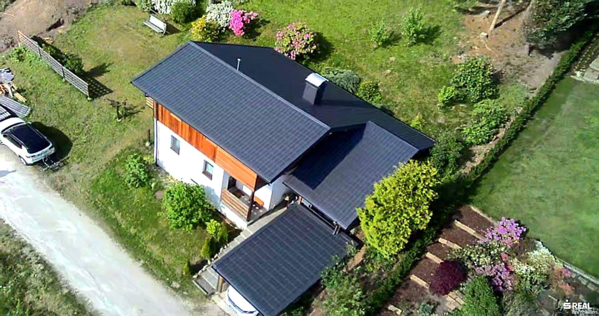 Dachaufsicht des Hauses mit dunklem Satteldach, umgeben von einem gepflegten Garten und einem Carport.