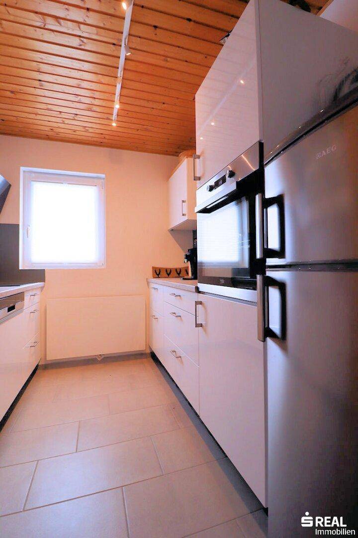 Moderne Küche mit weißen Hochglanzfronten, integrierten Geräten, Fliesenboden und einer Holzdecke.