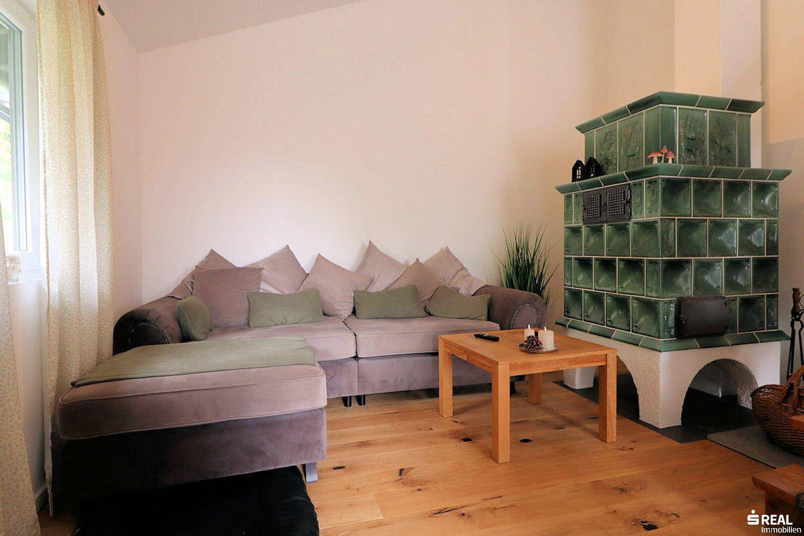 Gemütliches Wohnzimmer mit einem traditionellen grünen Kachelofen, Holzboden und einer bequemen Sitzecke.