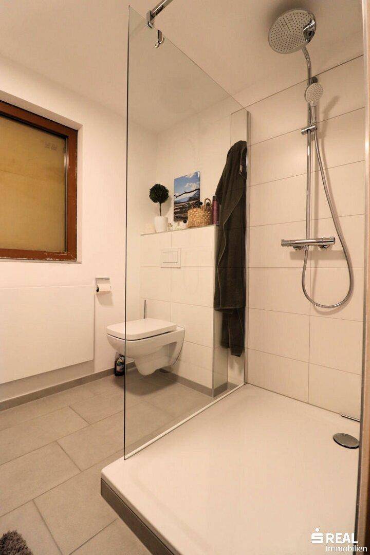 Helles, modernes Badezimmer mit ebenerdiger Glasdusche, wandhängendem WC und einem Fenster für Tageslicht.