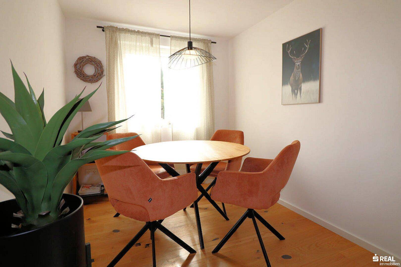 Einladender Essbereich mit einem runden Holztisch, modernen orangefarbenen Stühlen und hellem Holzboden.