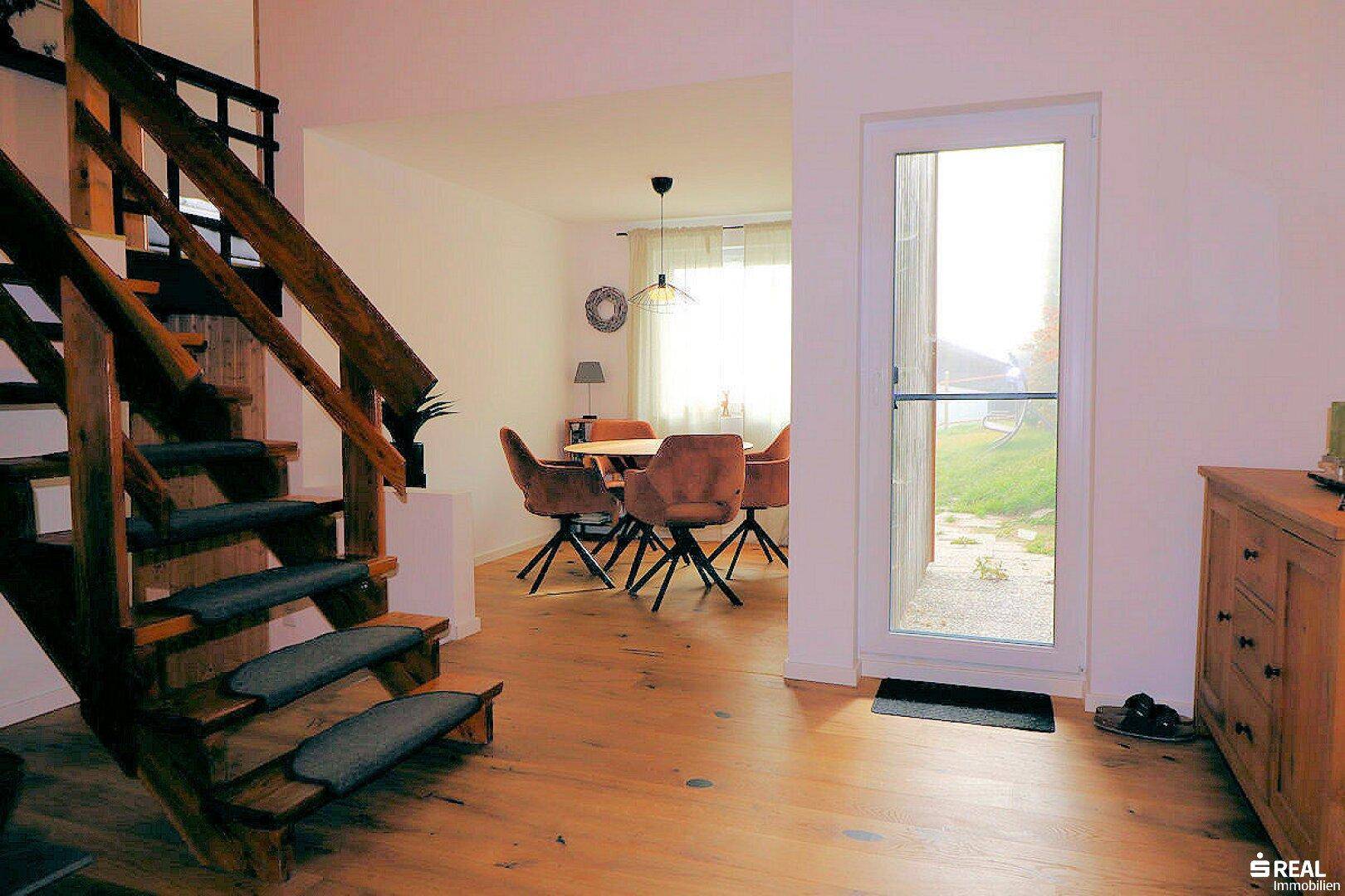 Eingangsbereich mit einer Holztreppe und direktem Blick in den hellen Essbereich mit Holzboden.