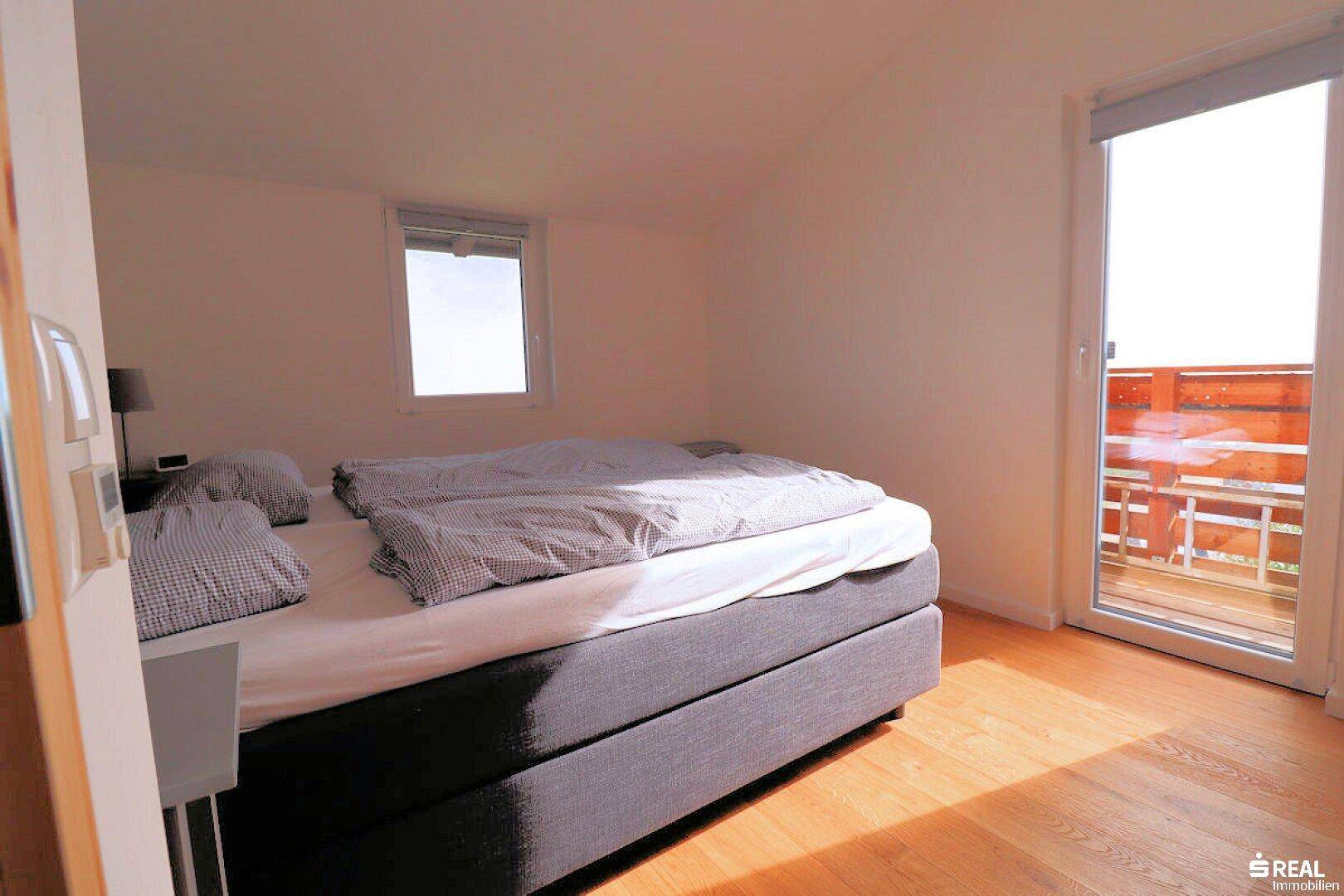 Helles Schlafzimmer mit Holzboden und einer großen Balkontür, die viel Tageslicht hereinlässt.