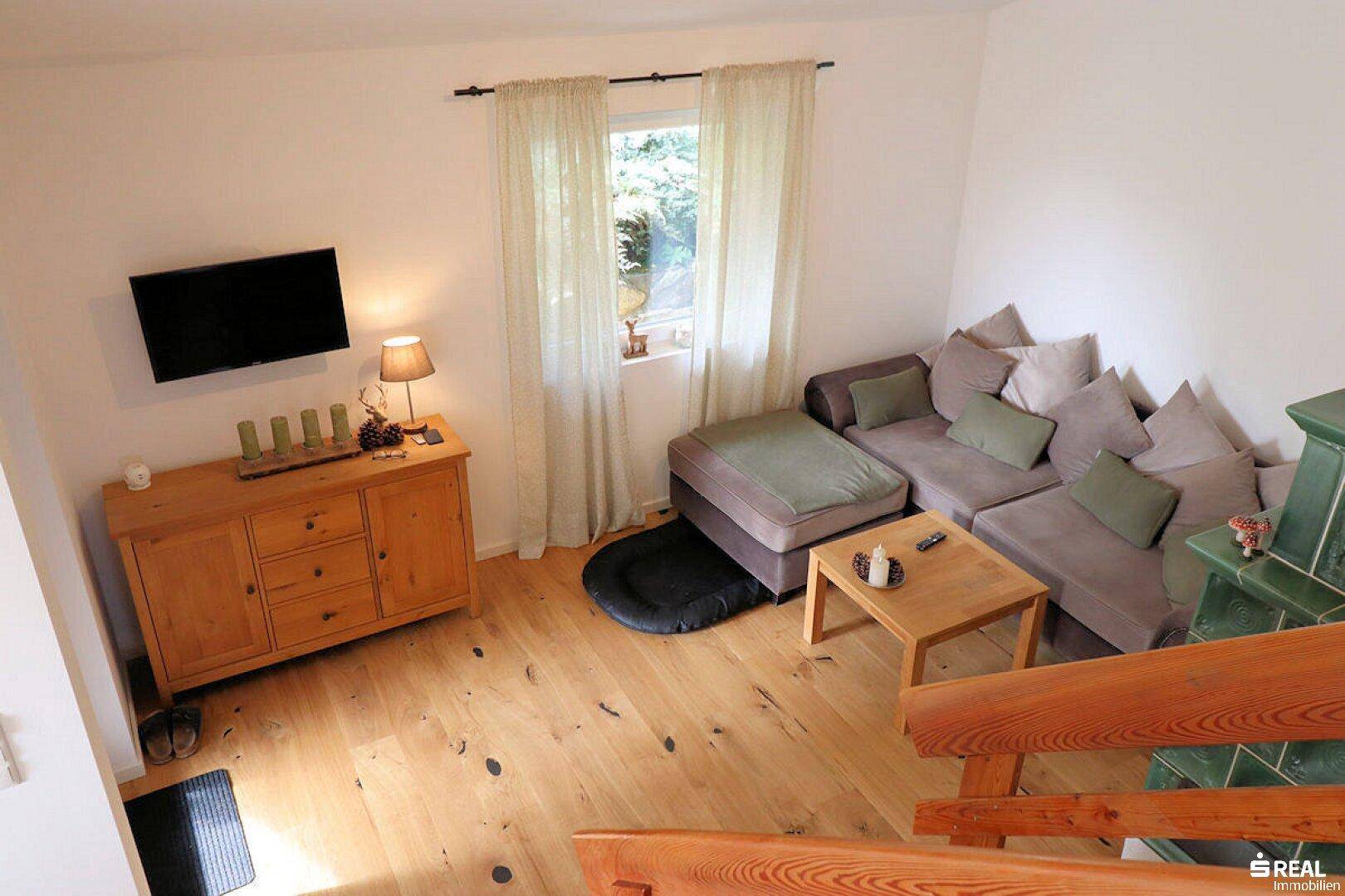 Blick von oben auf den Wohnbereich mit Sofa, Holzboden, einem Kachelofen und einem Fenster.