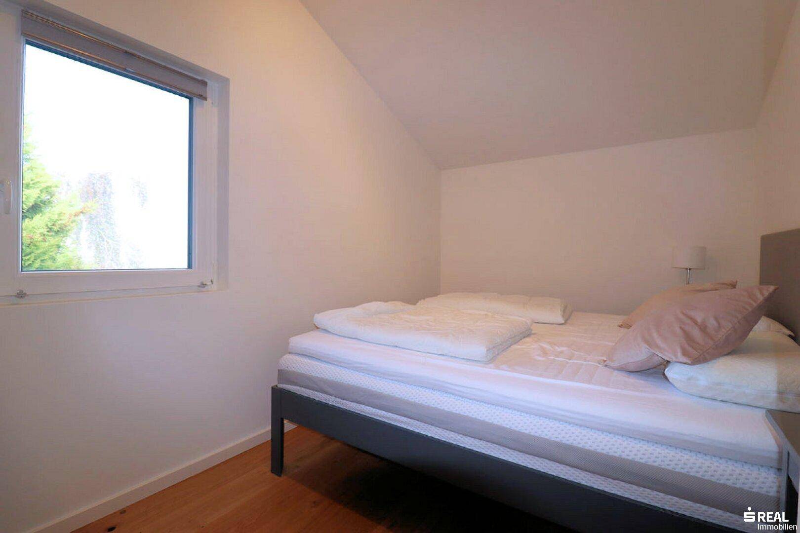 Gemütliches Schlafzimmer mit Holzboden und einem Fenster, das einen Blick ins Grüne bietet.