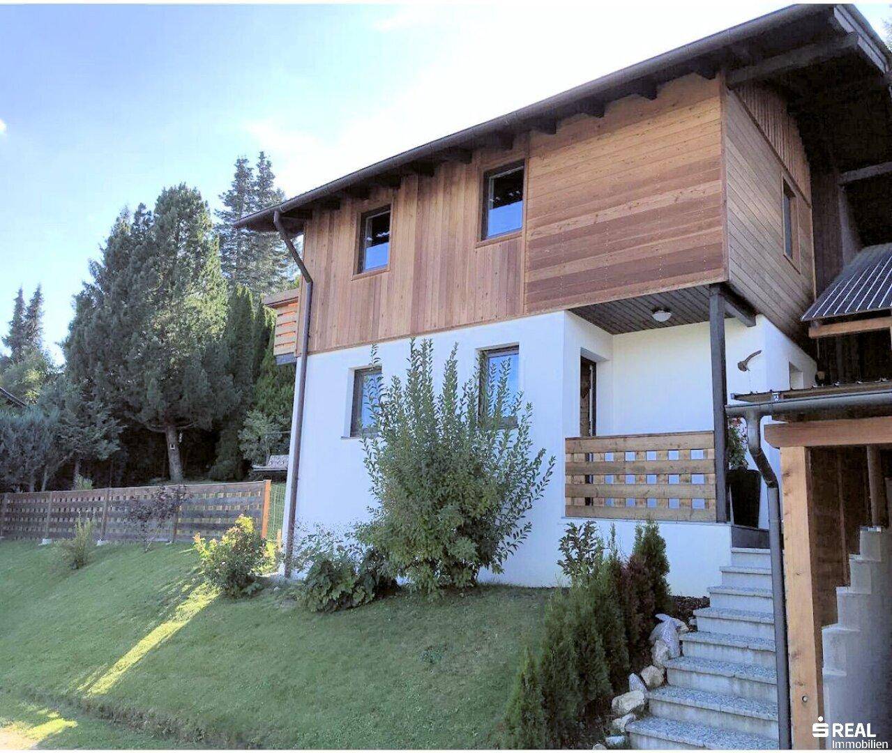 Seitenansicht des Hauses mit Holzverkleidung, weißem Putz und einer Steintreppe, die zum Eingang führt.