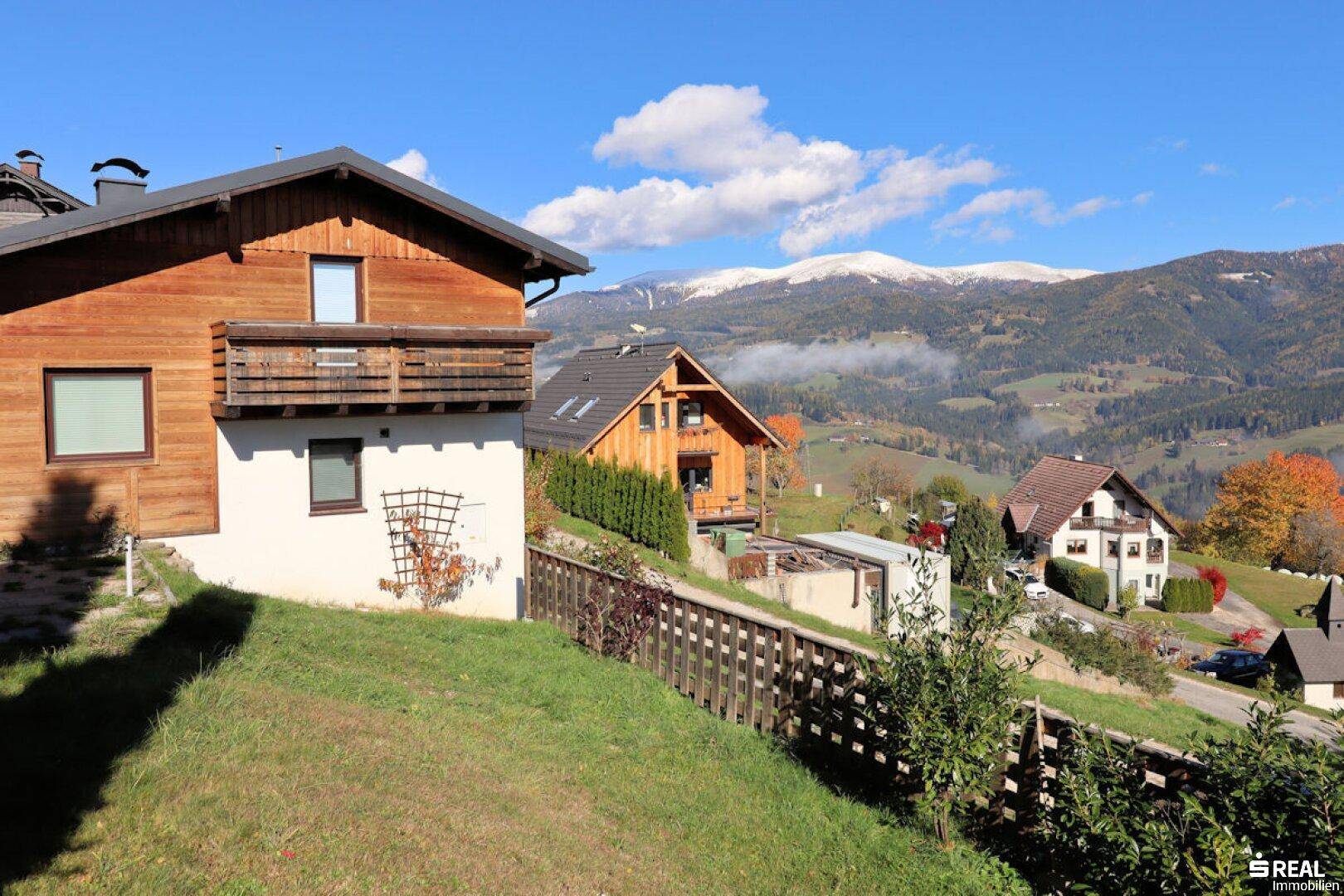 Das Haus mit Holzfassade bietet einen weiten Blick auf die umliegende Berglandschaft mit schneebedeckten Gipfeln.