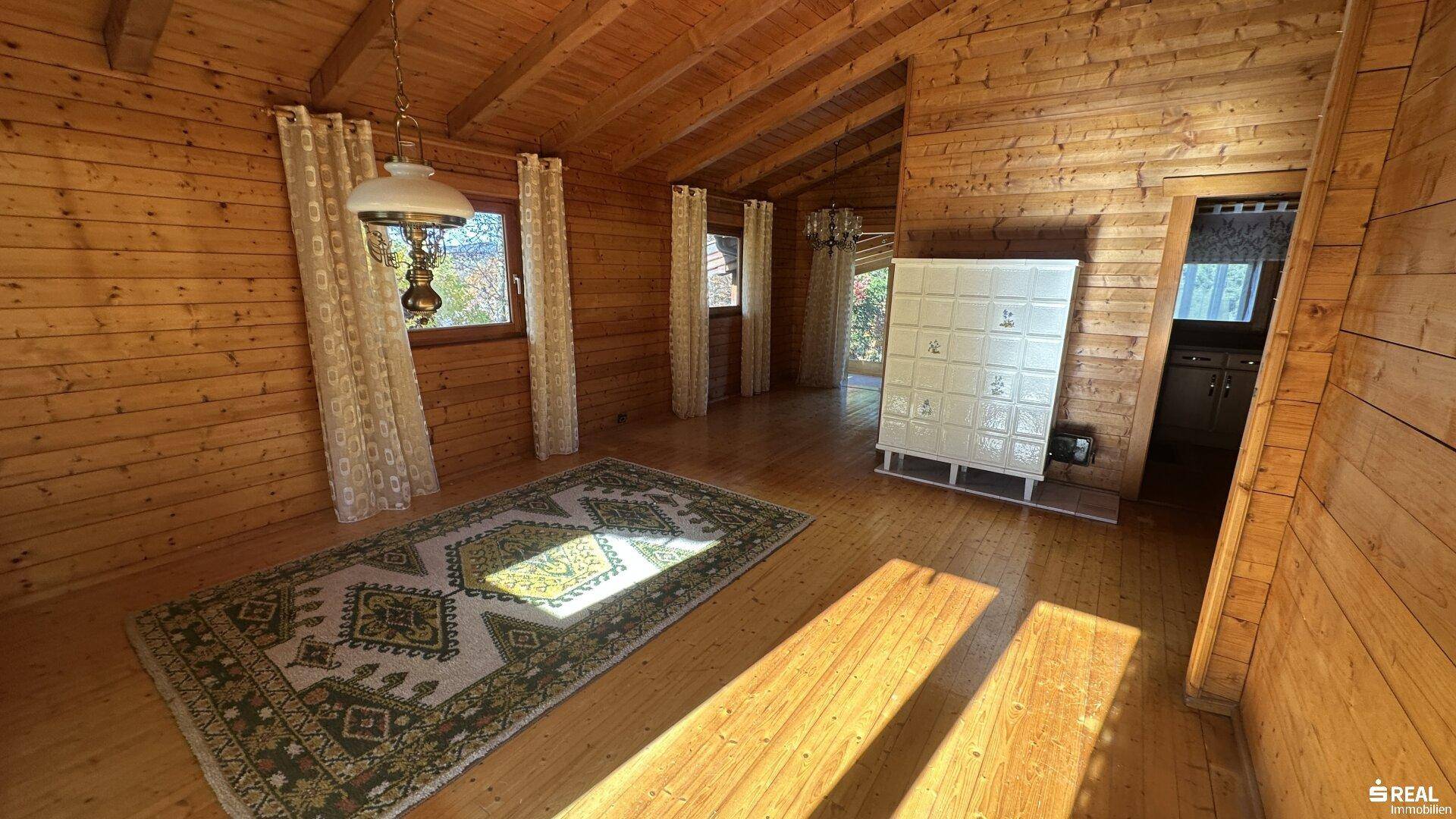 Gemütlicher Wohnraum mit Holzböden, Holzvertäfelung und traditionellem Kachelofen.