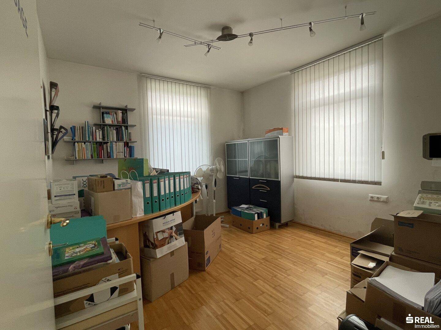 Geräumiges Büro oder Lagerzimmer mit Regalen und Fenstern, derzeit mit Umzugskartons gefüllt.