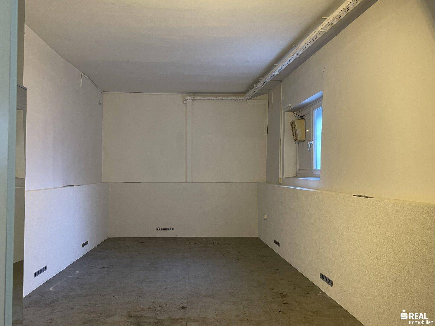 Schlichter Kellerraum mit Betonboden, kleinem Fenster und sichtbaren Installationen, ideal als Lagerfläche.