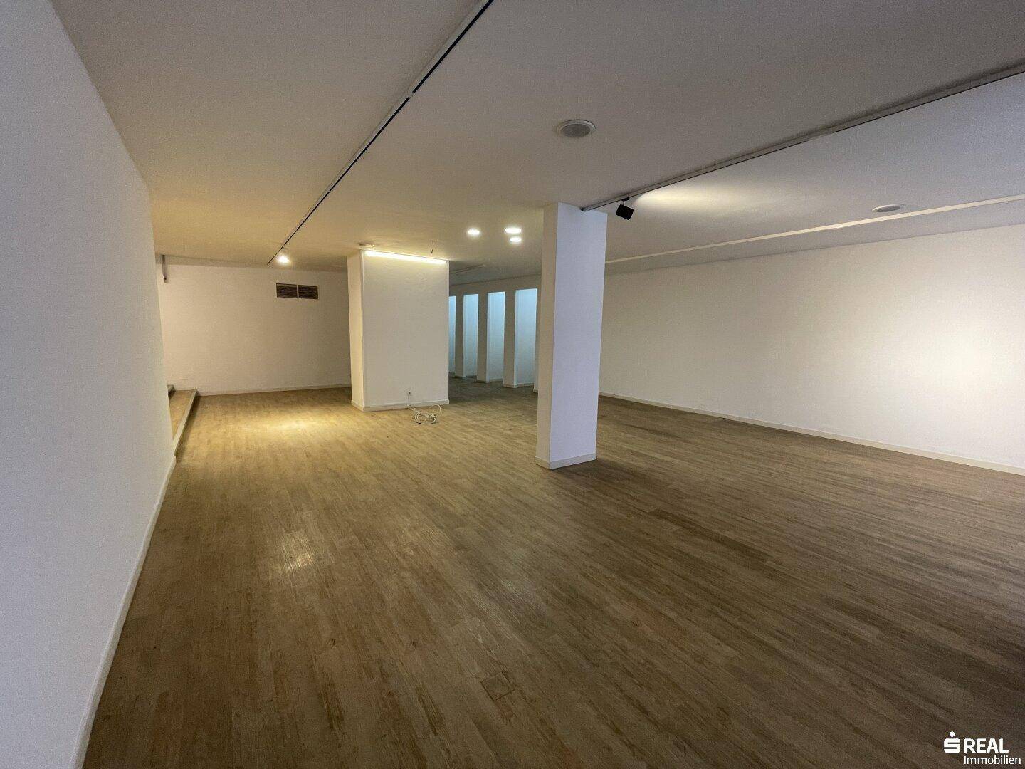 Heller Gewerberaum mit moderner Beleuchtung, Holzboden und weißen Wänden, ideal für flexible Nutzungskonzepte.